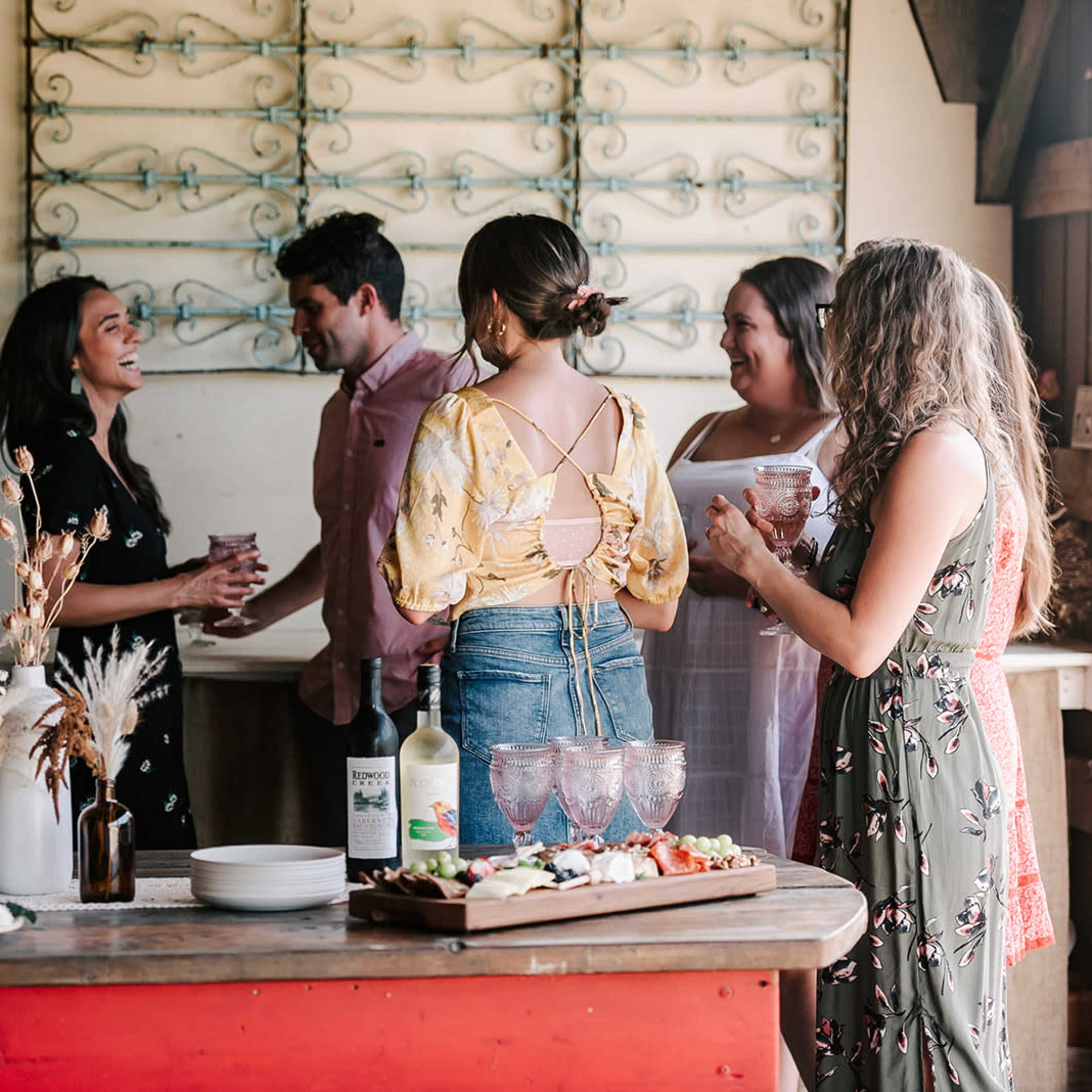 A group of five people socialize around a table with drinks and food in a brightly lit indoor setting.