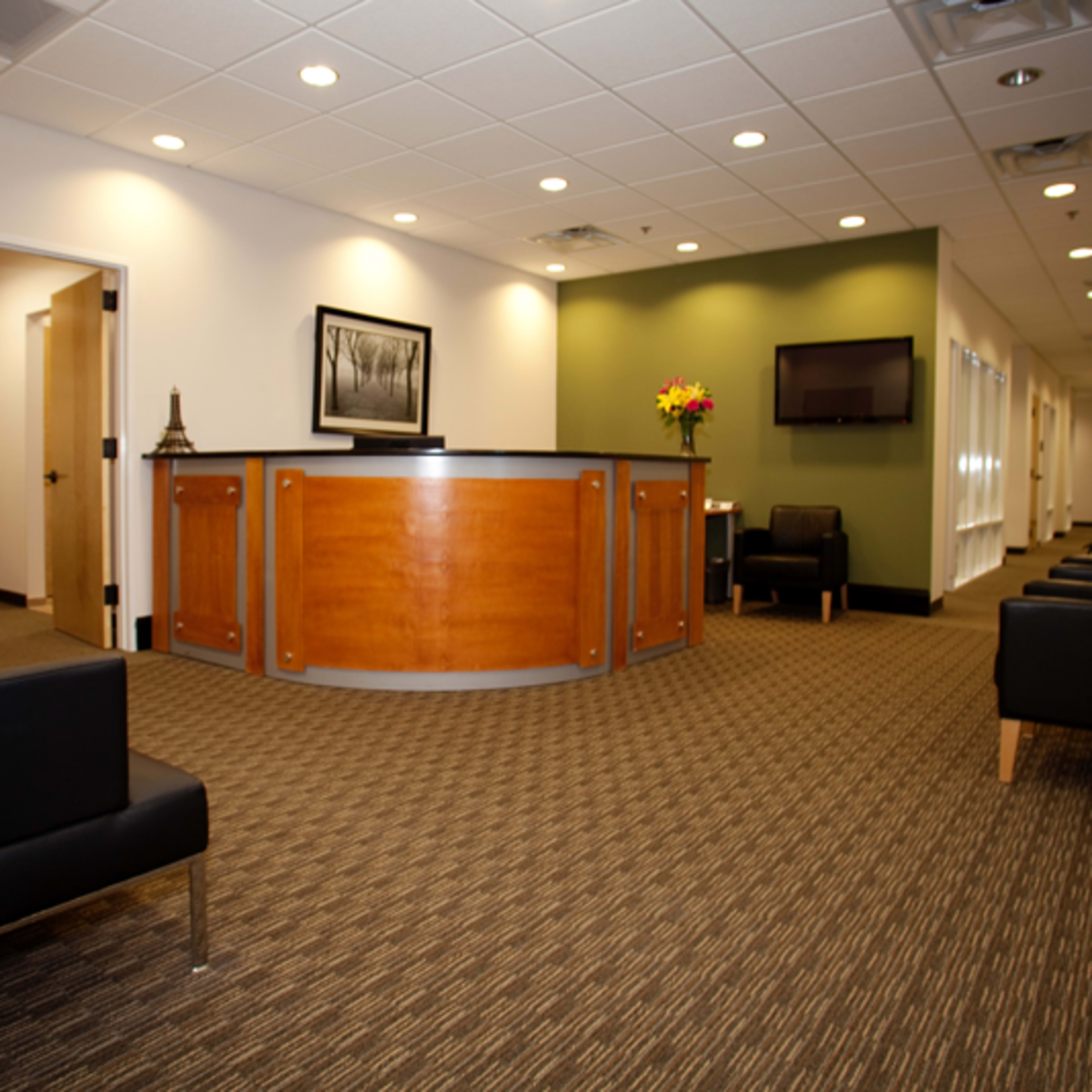 A modern reception area with a wooden front desk, black chairs, and green accent walls.