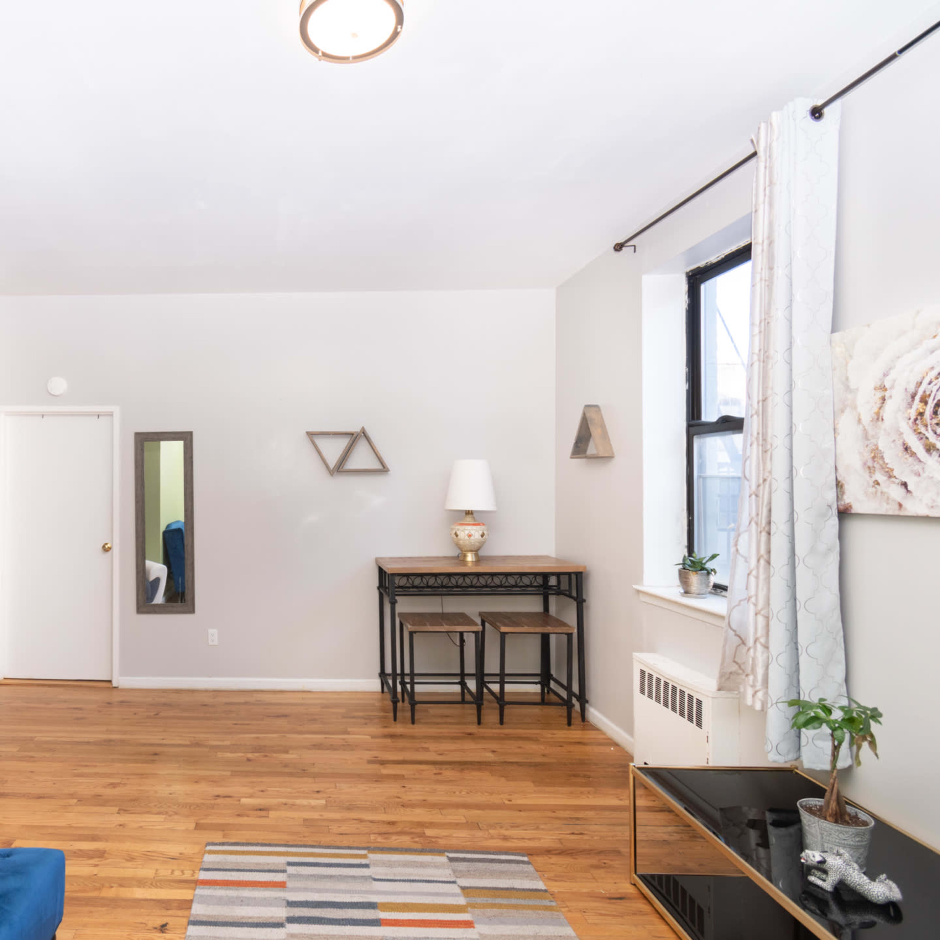 The living room features a blue sofa, a mirror, a small table with chairs, and wooden flooring, with green and gray walls.