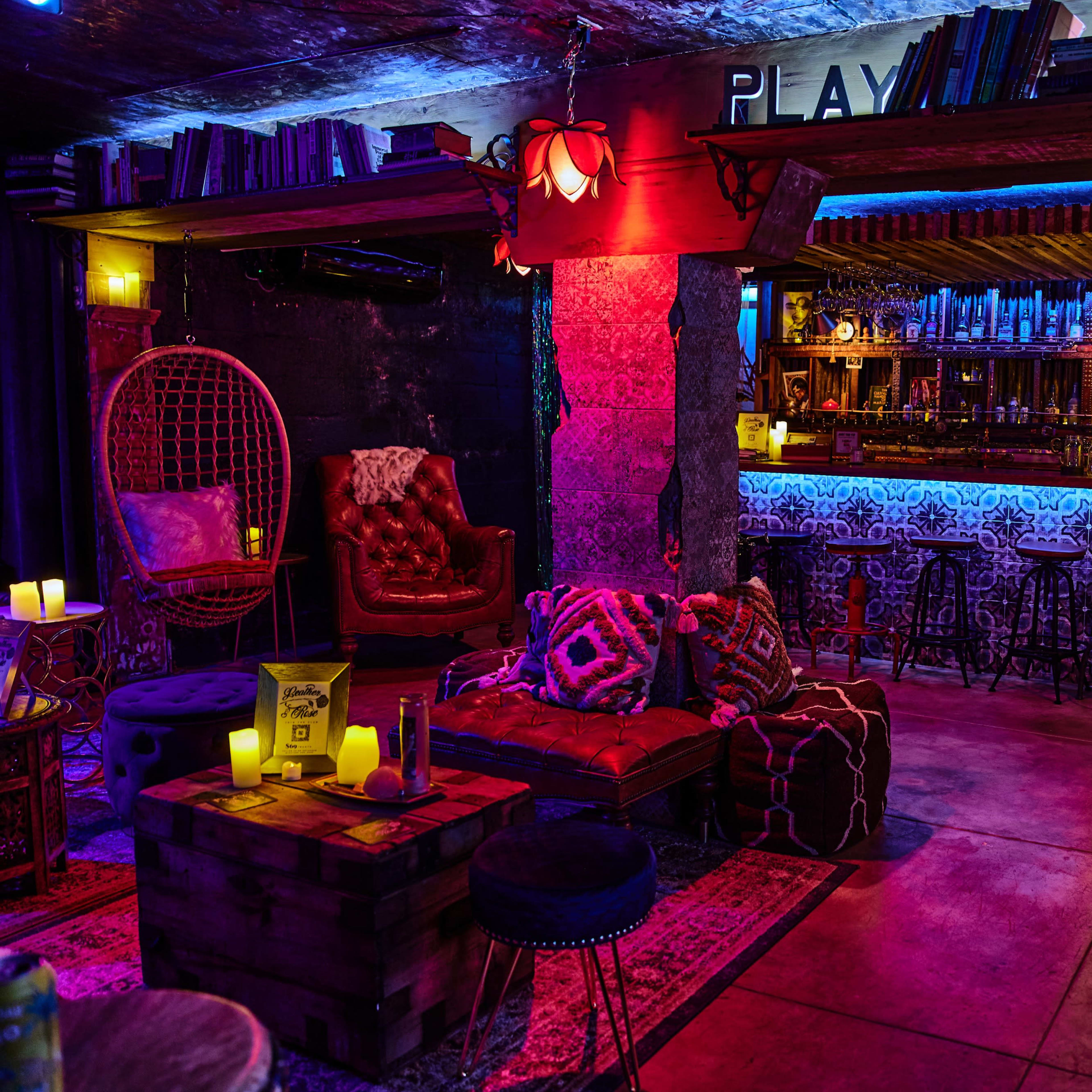 A colorful bar interior with cozy seating, ambient lighting, and a variety of decorative elements, including books and candles.