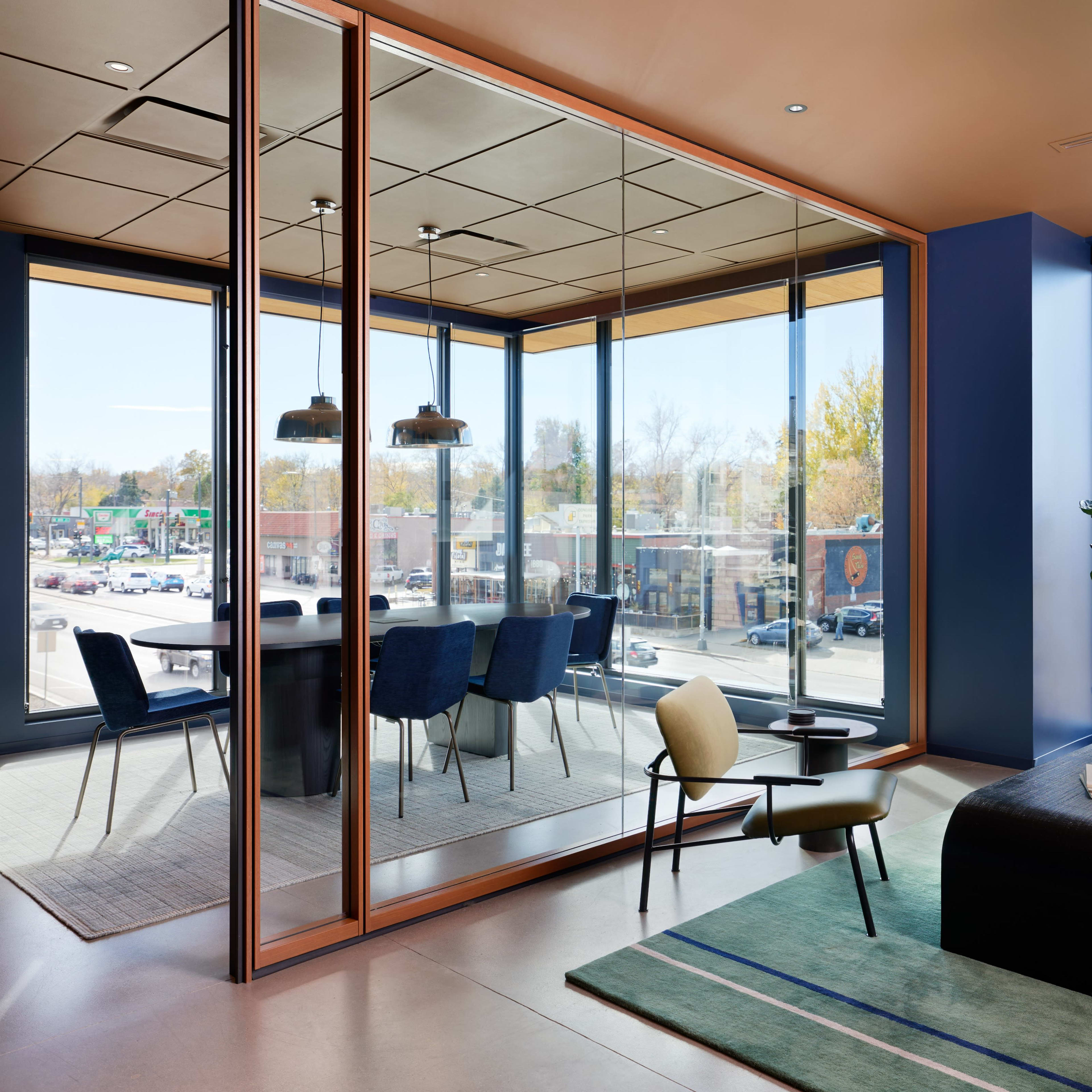 A modern office interior with a glass-walled meeting room, a seating area, and a view of an outdoor parking lot.