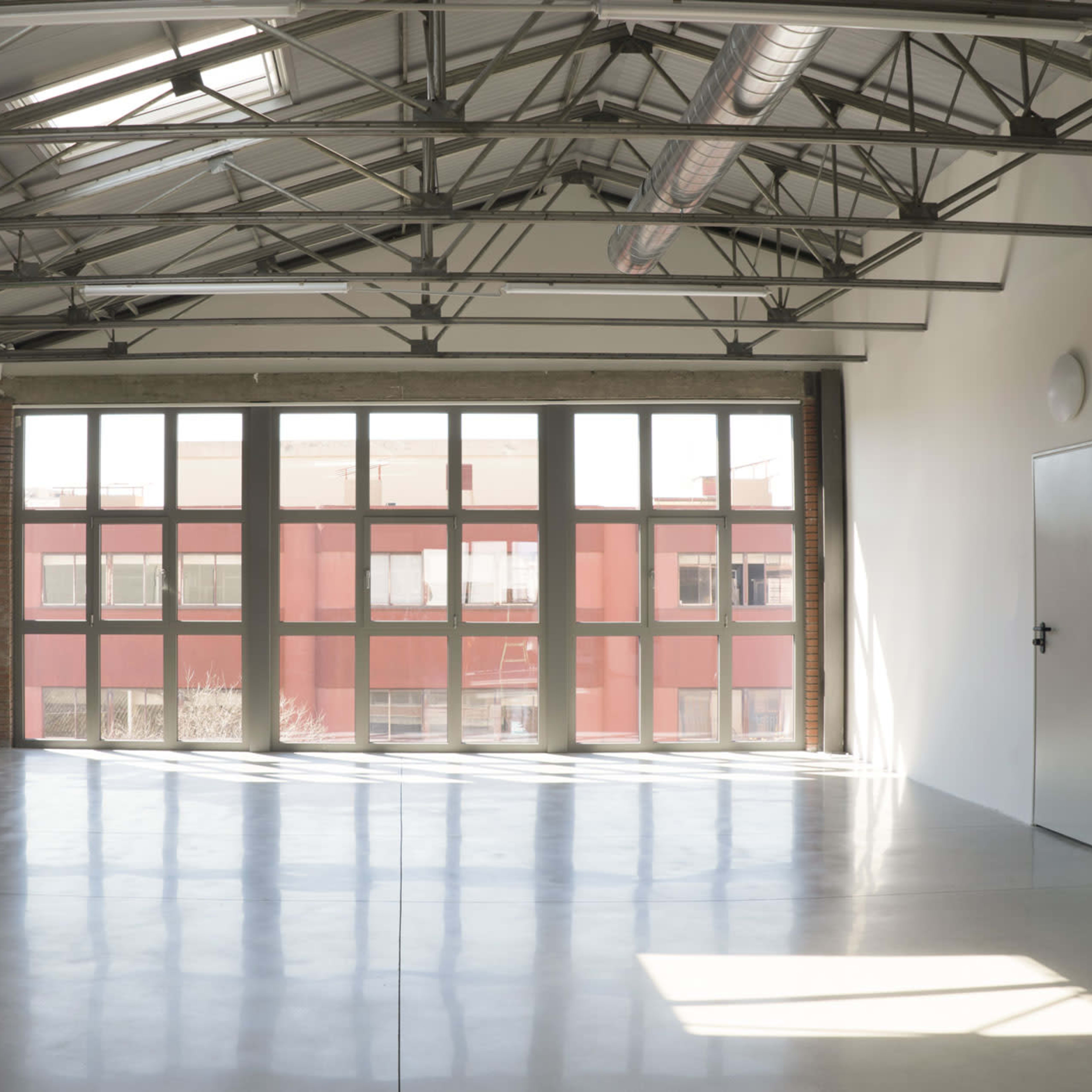 An empty room with large windows, high ceilings, and polished concrete flooring.