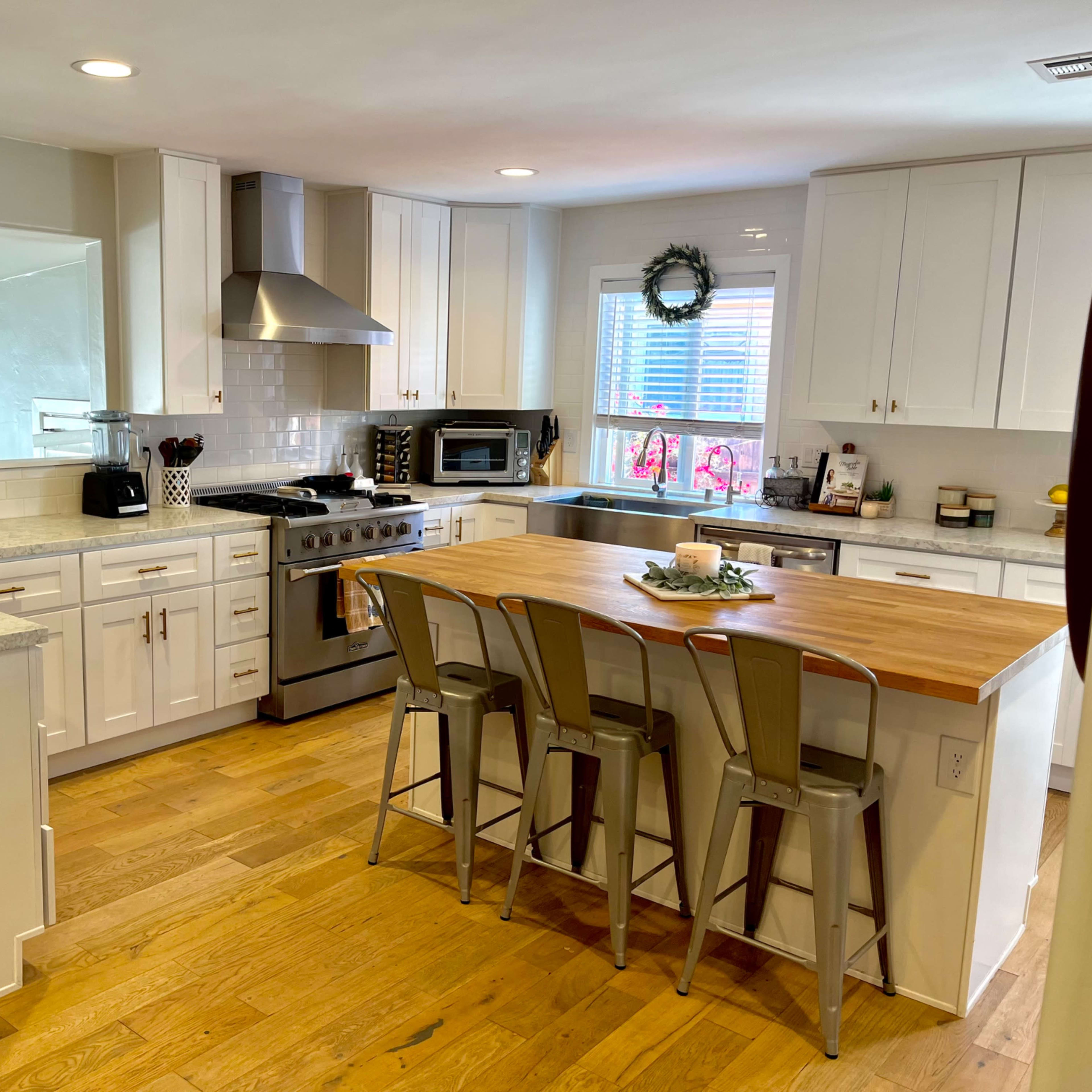 The kitchen features white cabinets, a wooden island with metal stools, and modern appliances.