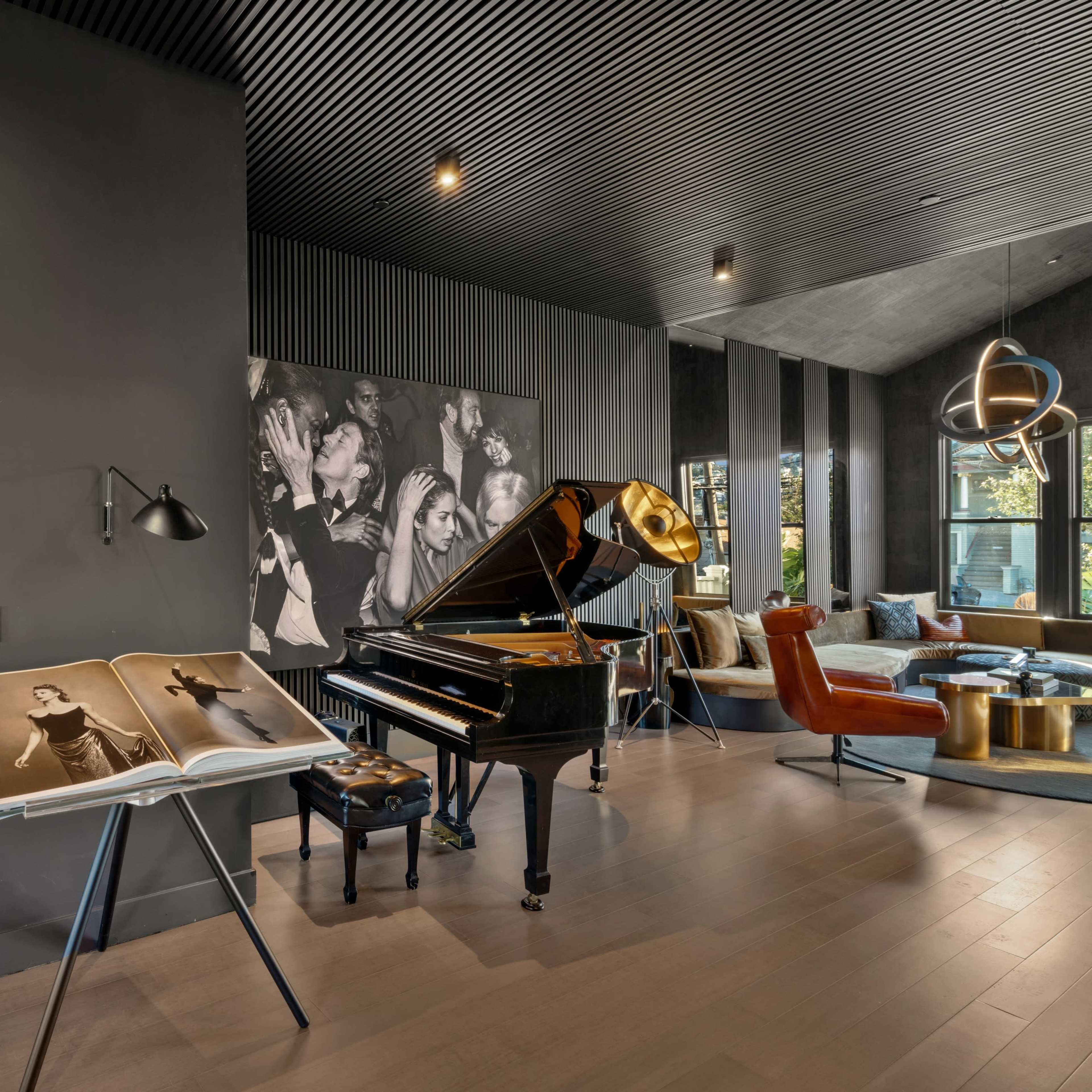 A grand piano stands next to a large open photo book and is accompanied by a wall adorned with black-and-white photographs in a stylish living space.