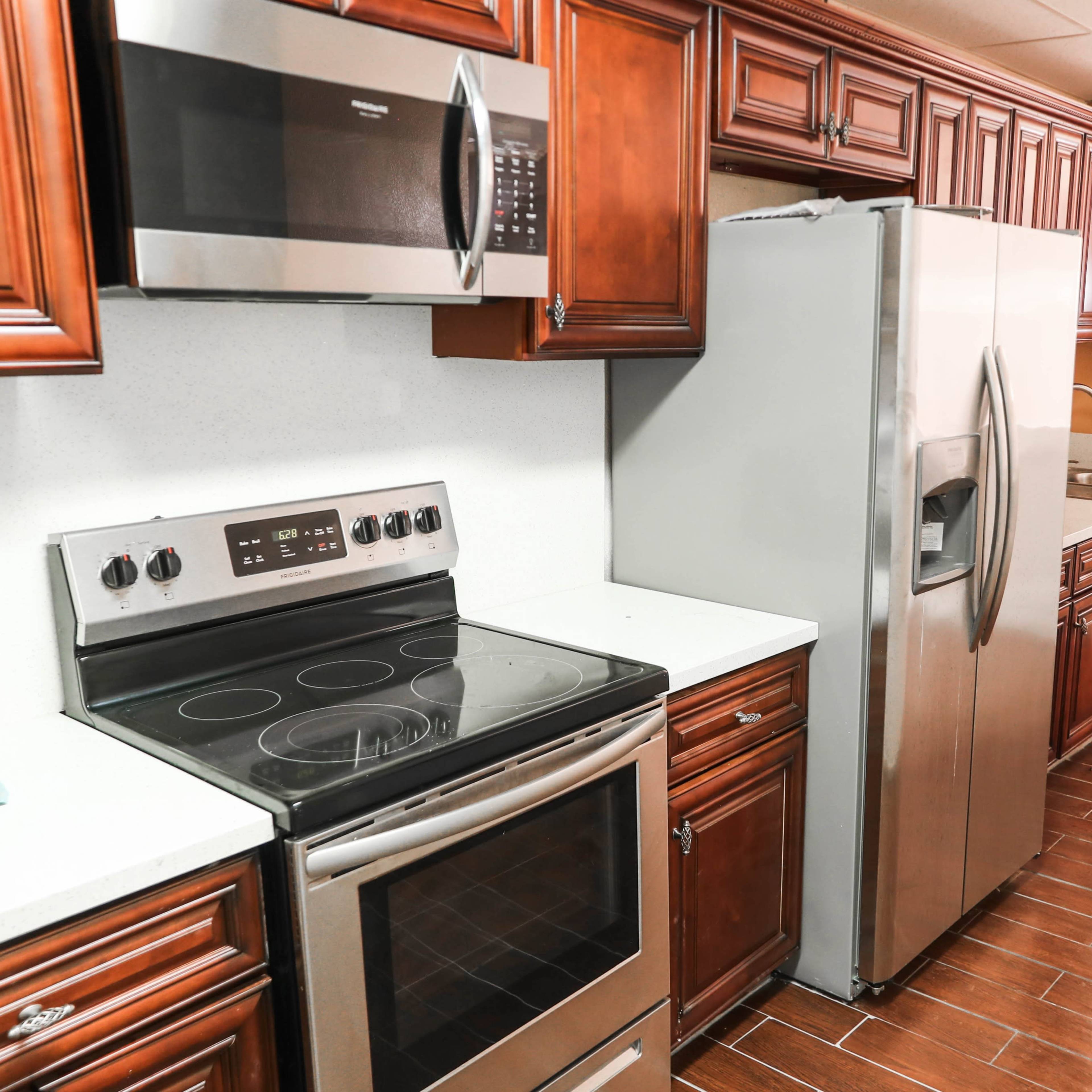 A kitchen featuring wooden cabinets, a stainless steel refrigerator, an electric stove, and a microwave, with wood-like flooring.