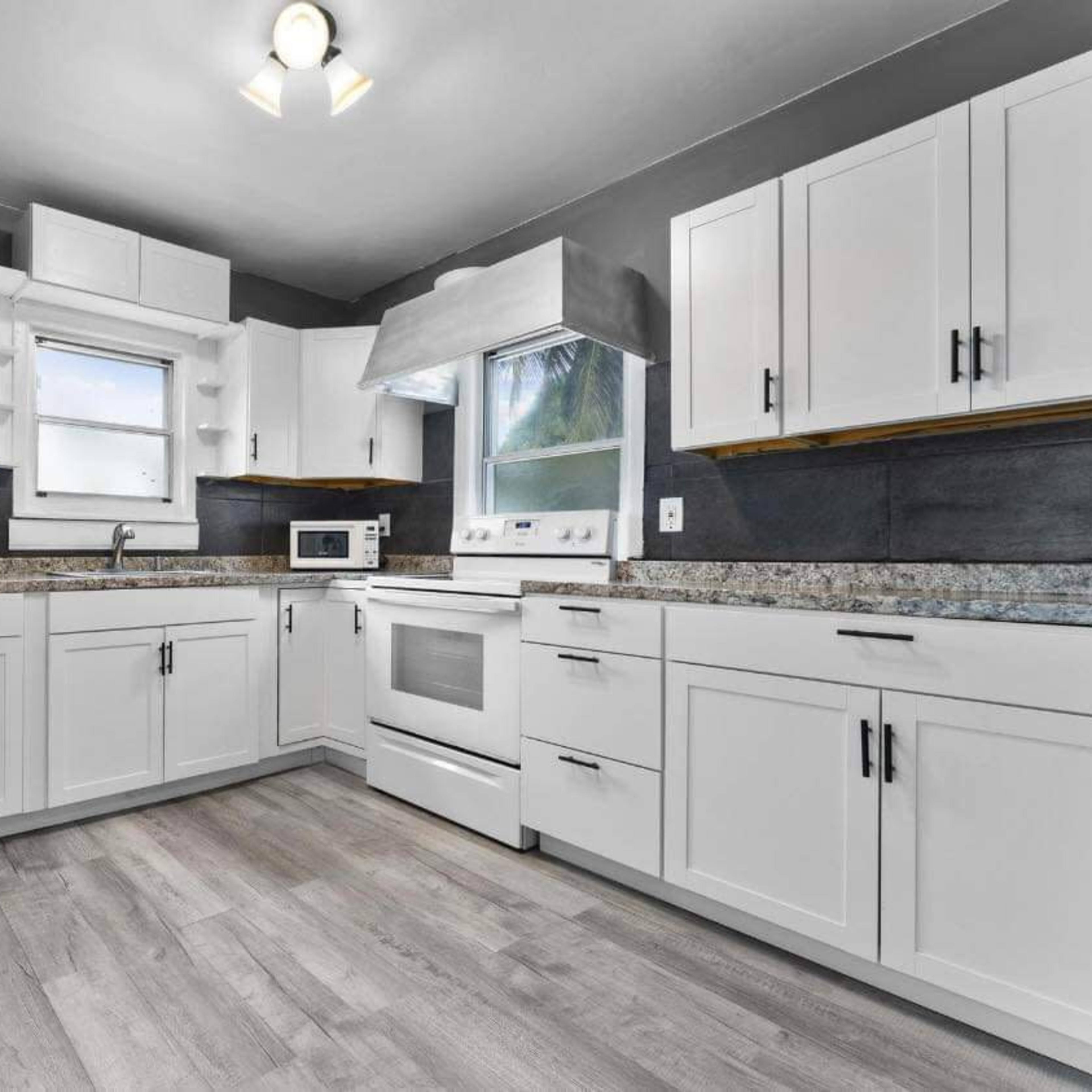 The kitchen features white cabinets, granite countertops, and modern appliances, with a window providing natural light.