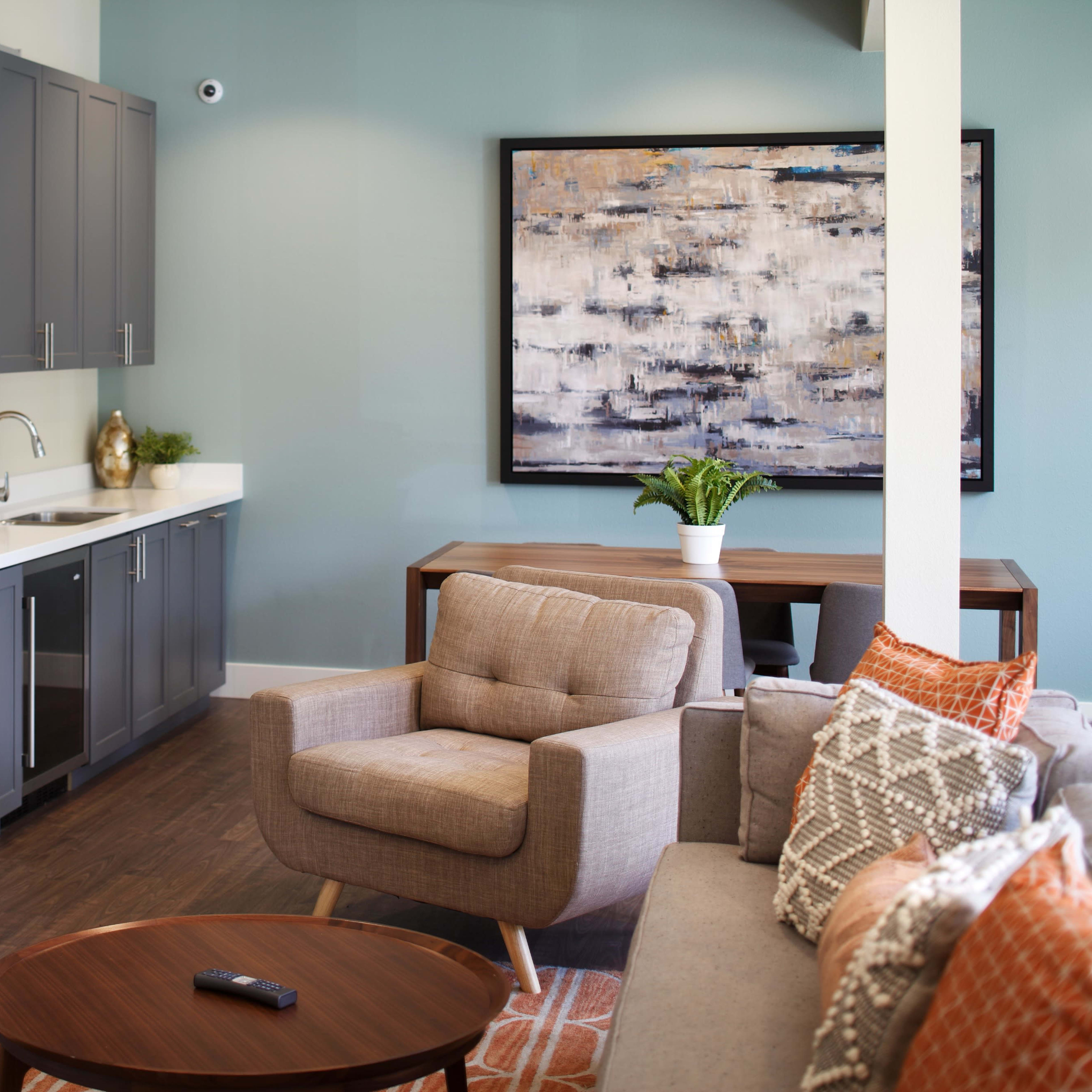 A modern living space featuring a gray kitchen cabinet area, a cozy seating arrangement, and a table with a decorative painting on the wall.