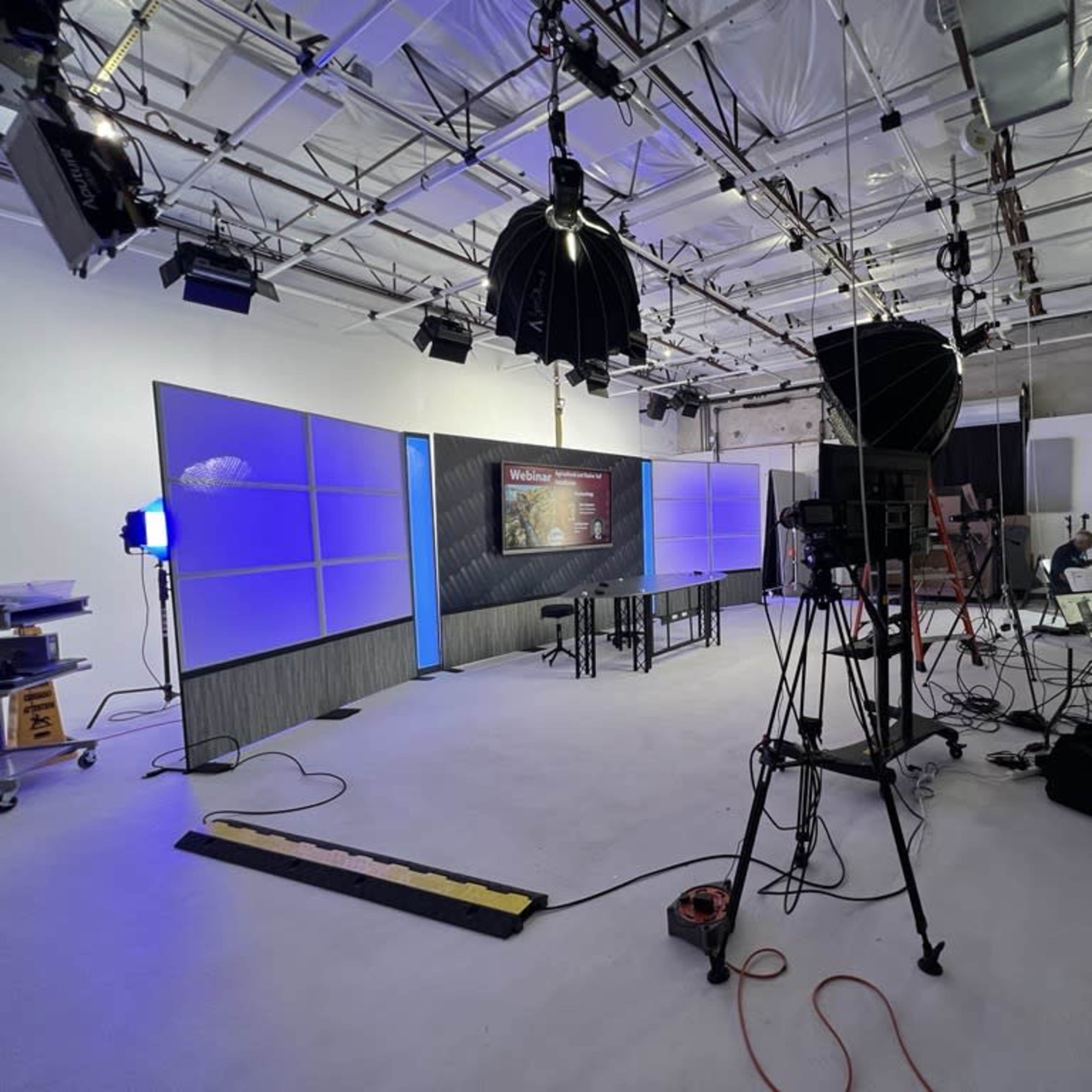 A photography studio with multiple lights, cameras, and a large backdrop, equipped for a video production setup.