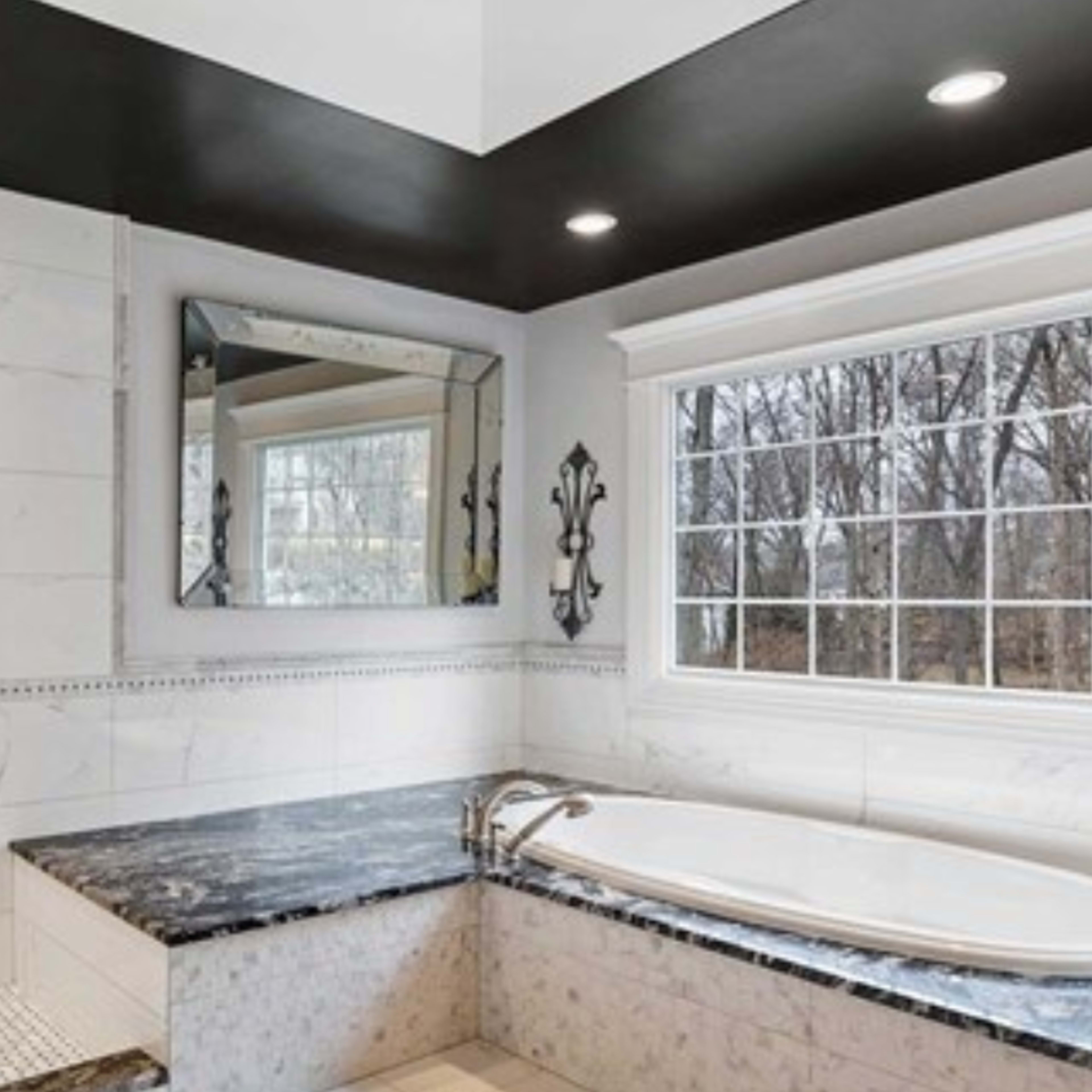 A modern bathroom featuring a large bathtub, a separate shower area, and a window providing natural light, accented by marble tiles and dark cabinetry.