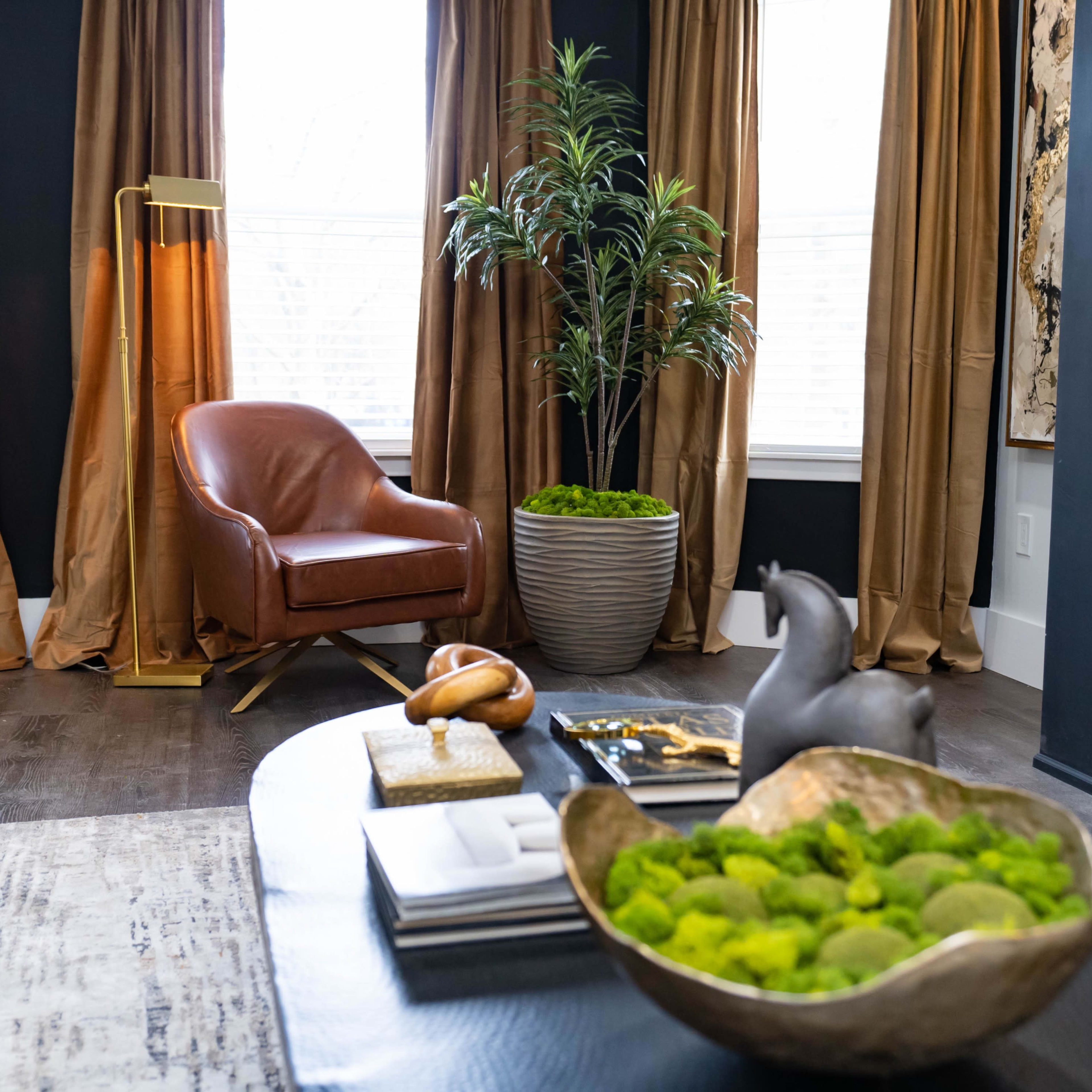 A cozy living room featuring a brown leather chair, a potted plant, and a coffee table adorned with decorative items and a bowl of green moss.