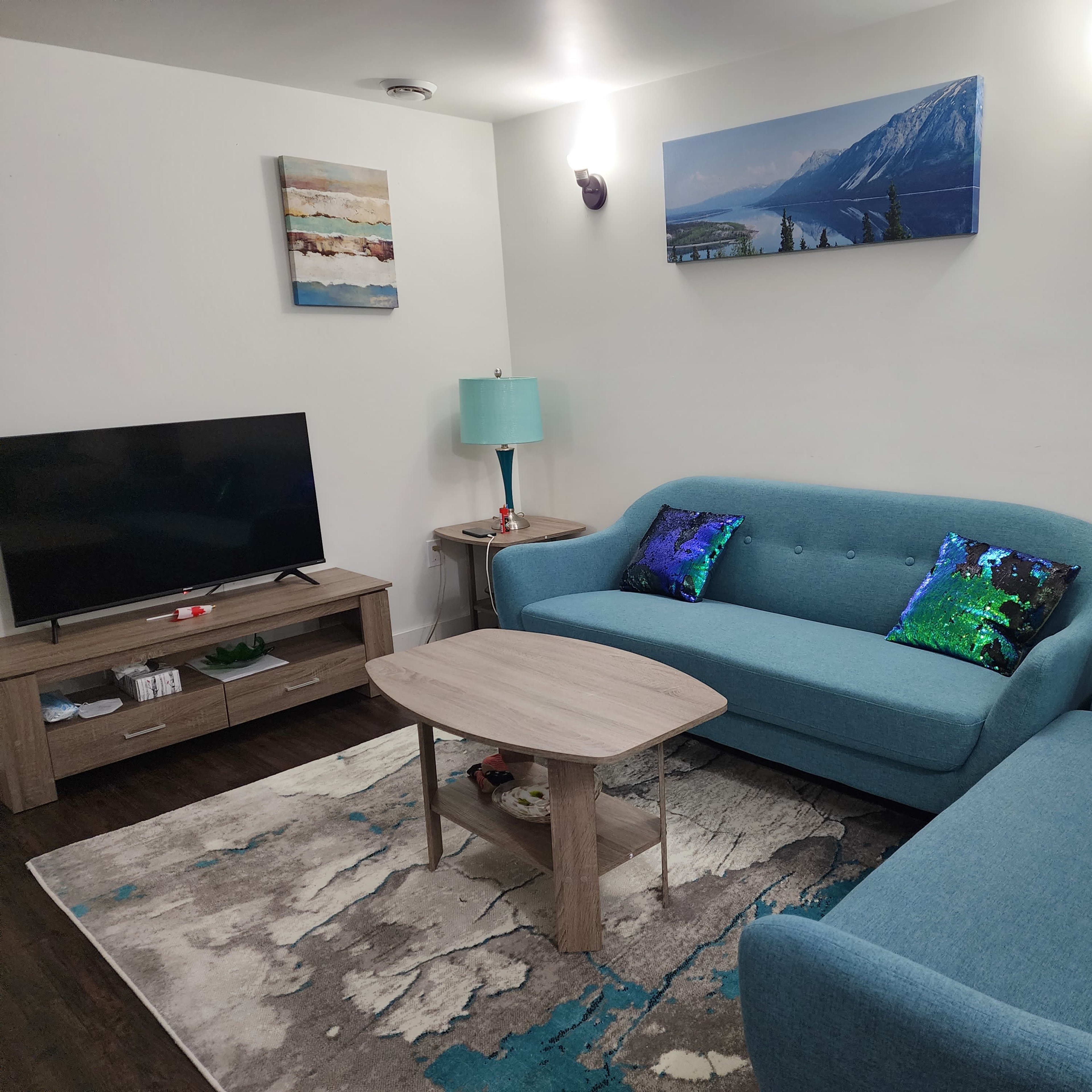 A modern living room featuring a blue couch, a matching armchair, a coffee table, a television on a media console, and decorative wall art.