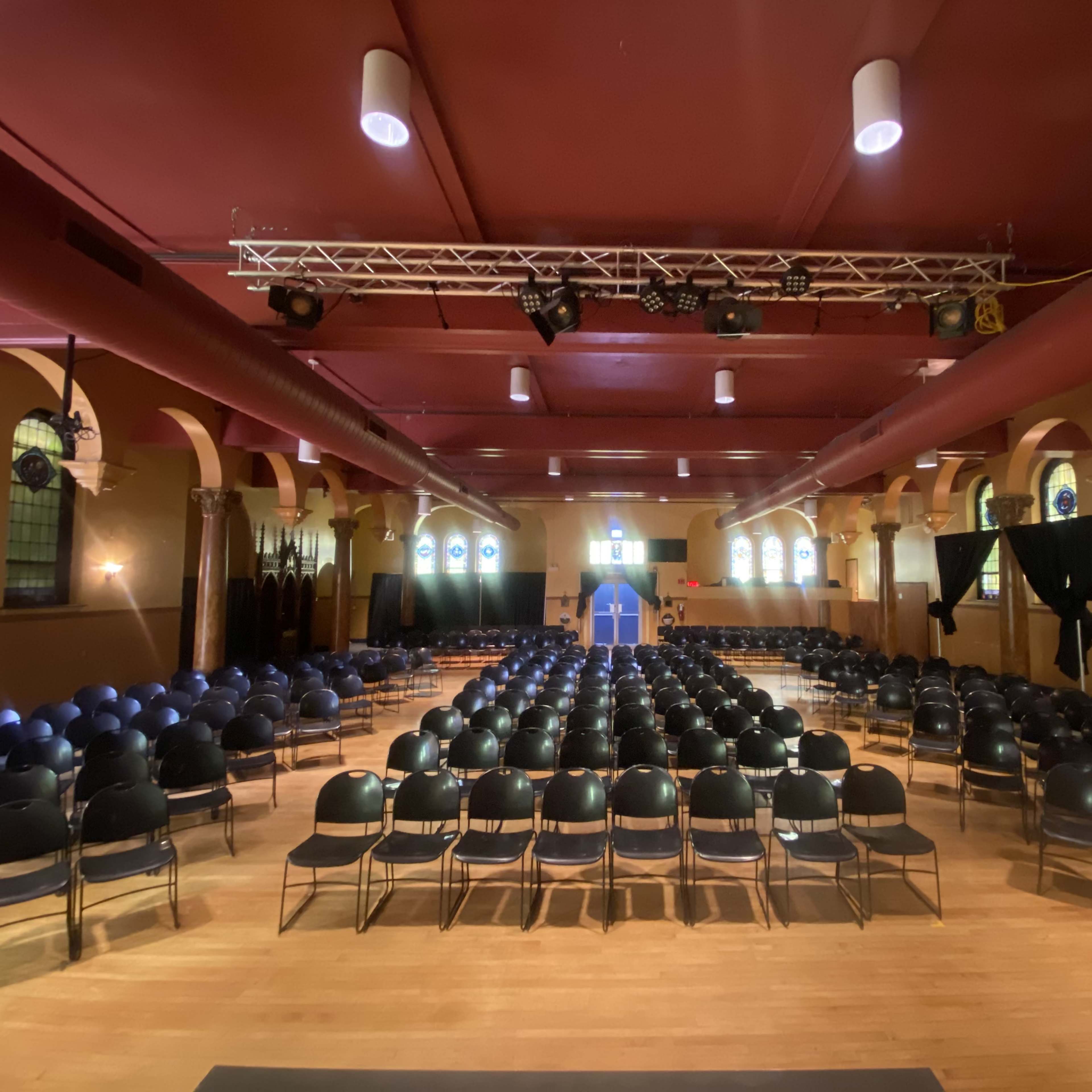A large indoor hall arranged with rows of black chairs facing a stage at the front.