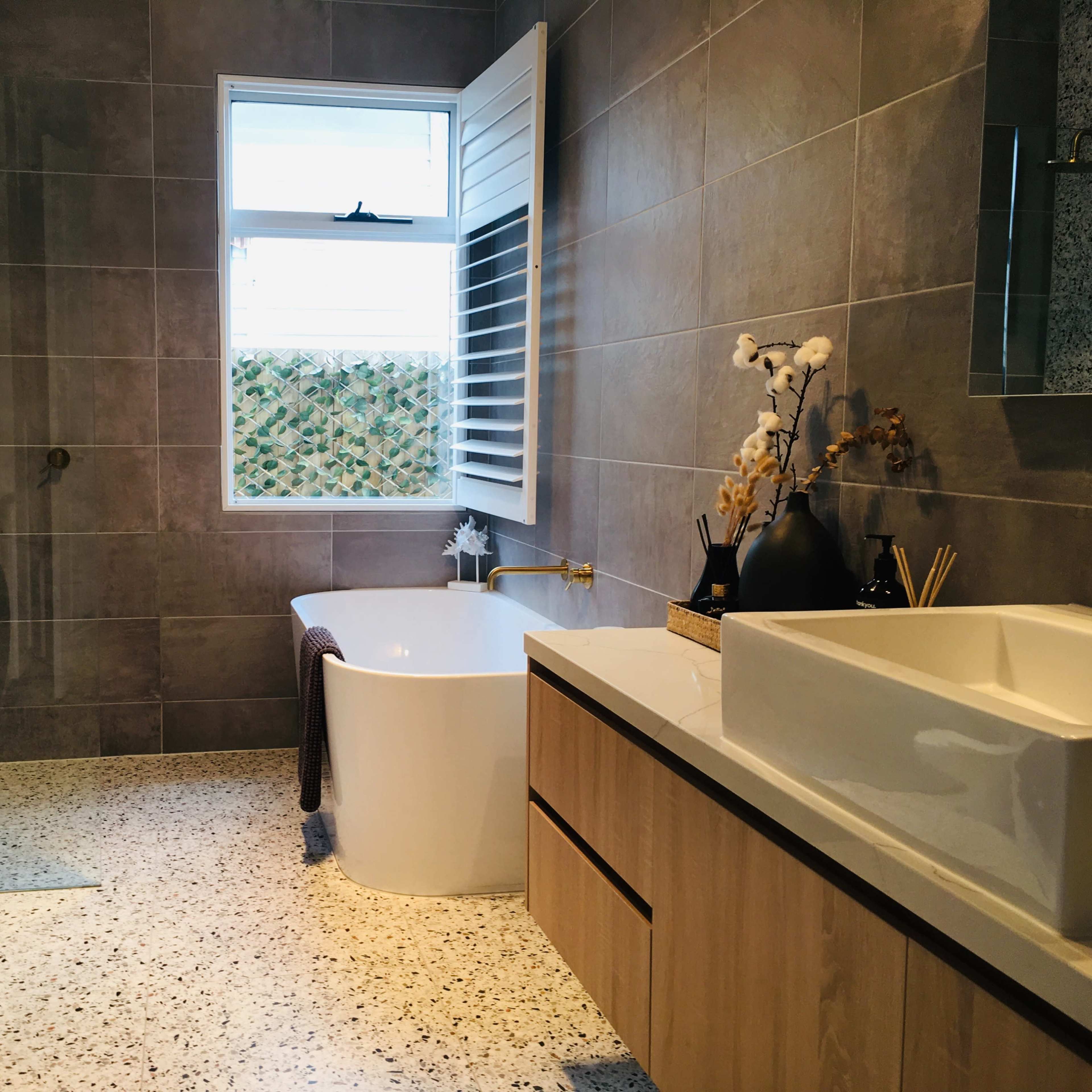 The modern bathroom features a freestanding bathtub, a washer/dryer unit, a sink with a wooden vanity, and a window with decorative shutters.