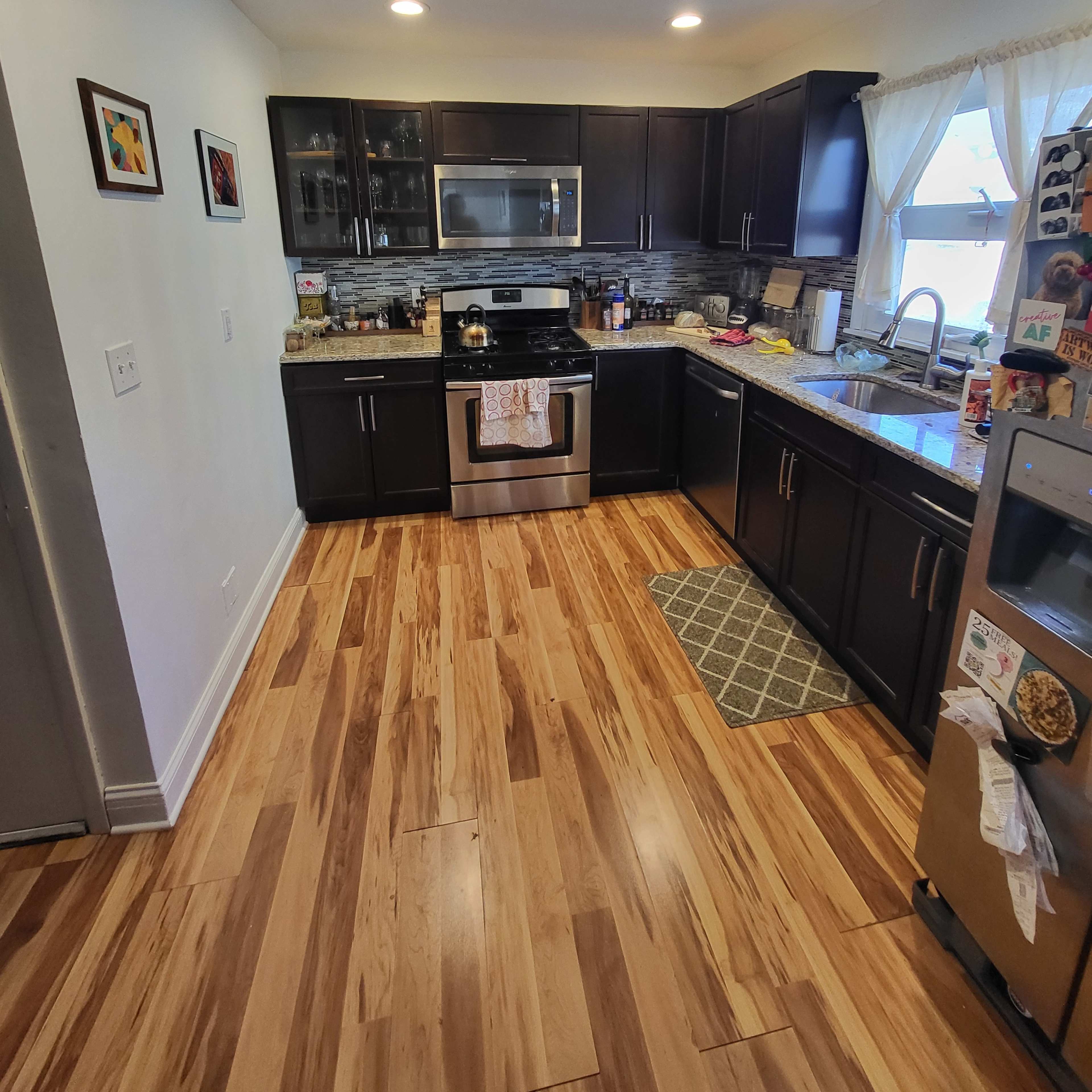 A modern kitchen with dark cabinets, stainless steel appliances, and wooden flooring.
