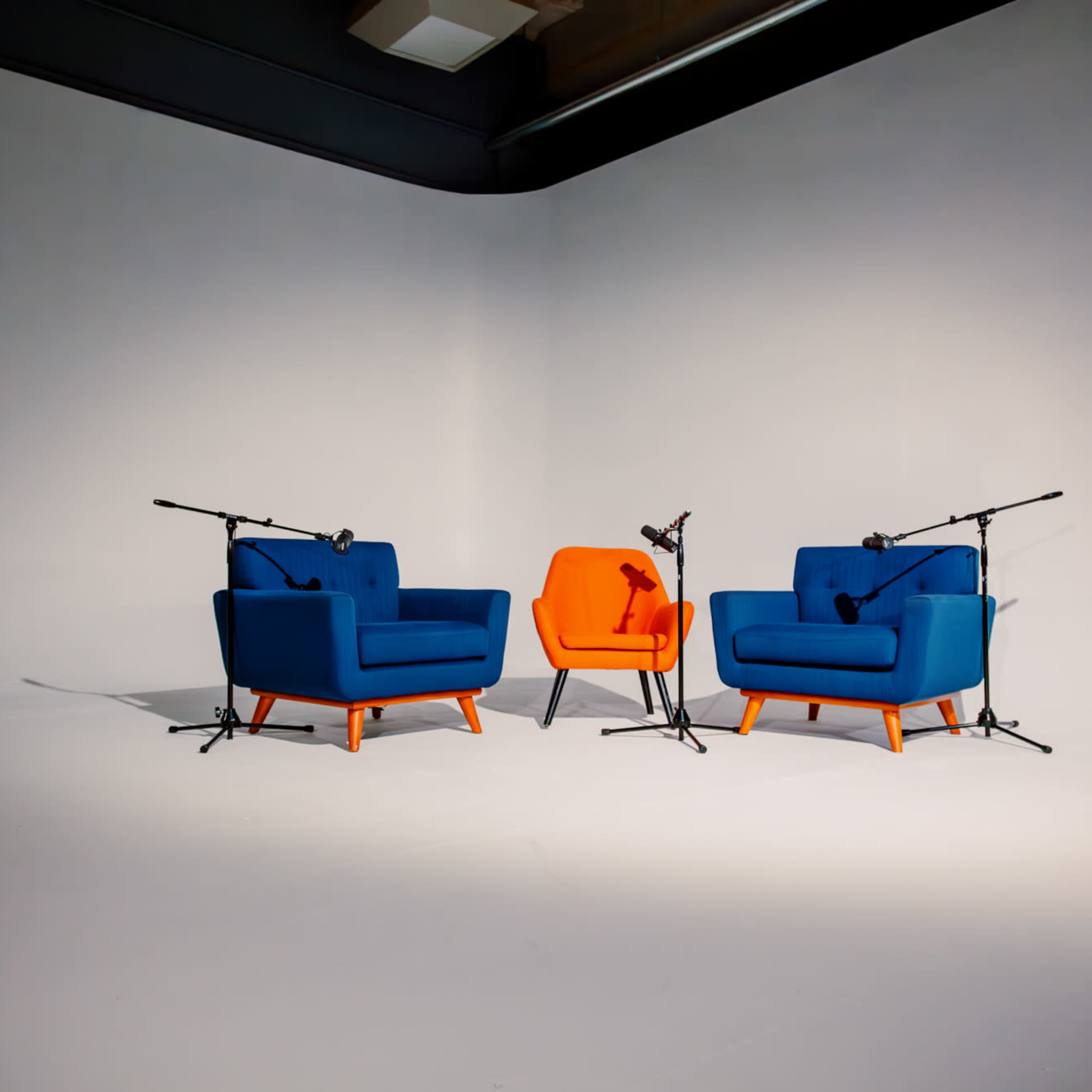 Two armchairs, one blue and one orange, positioned in a minimalist room with microphones mounted on stands.