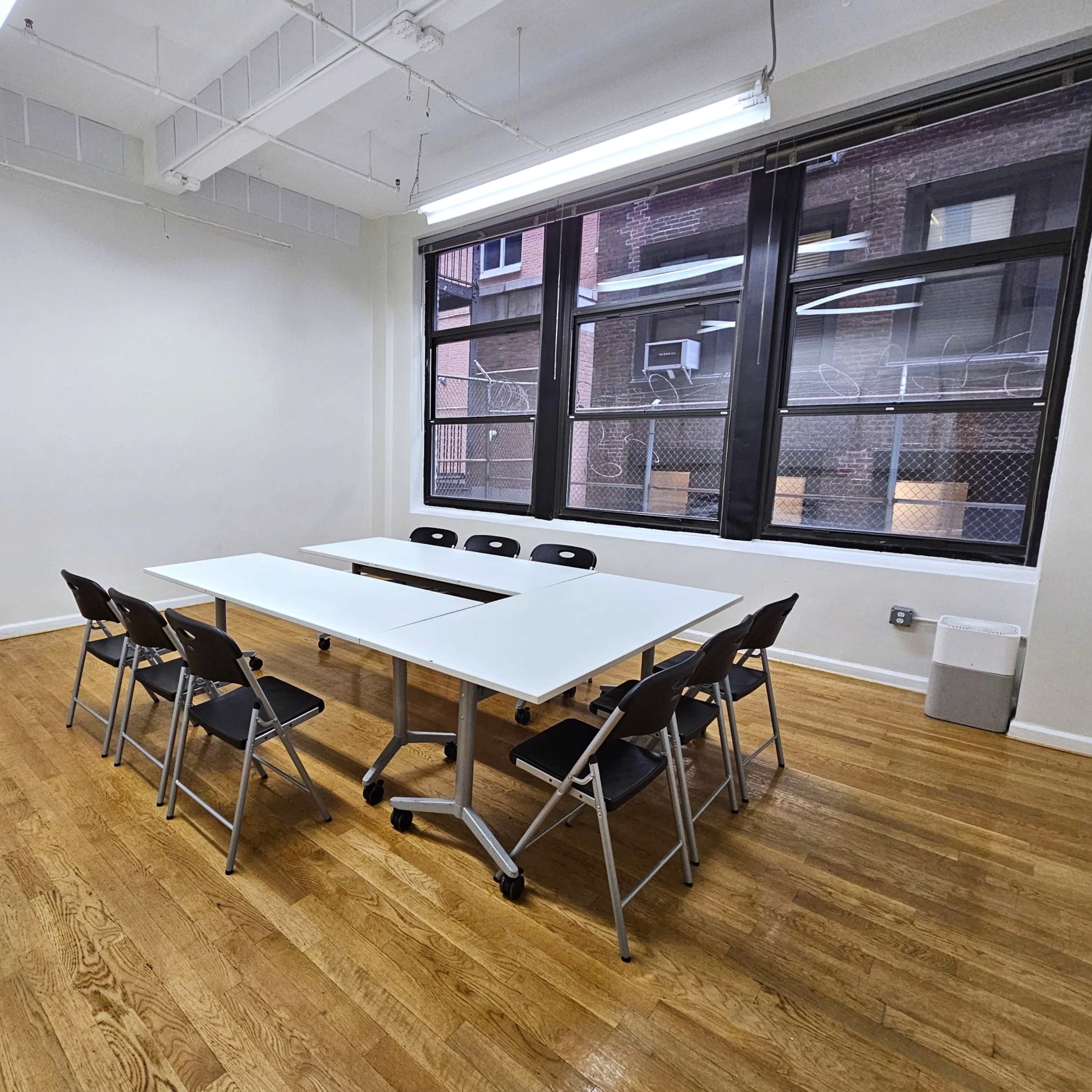 A conference room with a large table surrounded by black chairs and windows overlooking an urban exterior.