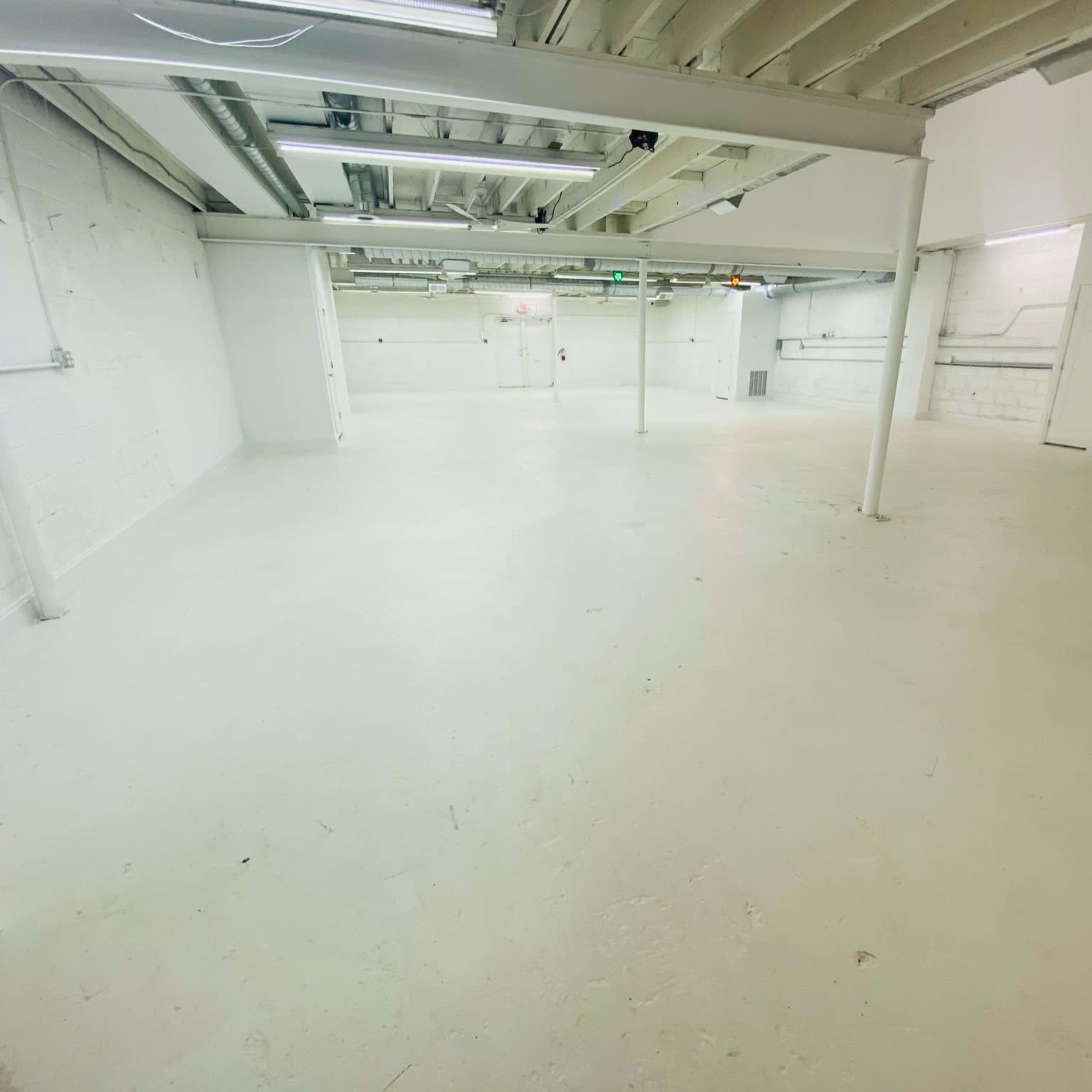 A spacious, empty warehouse interior with a white floor and exposed ceiling beams.
