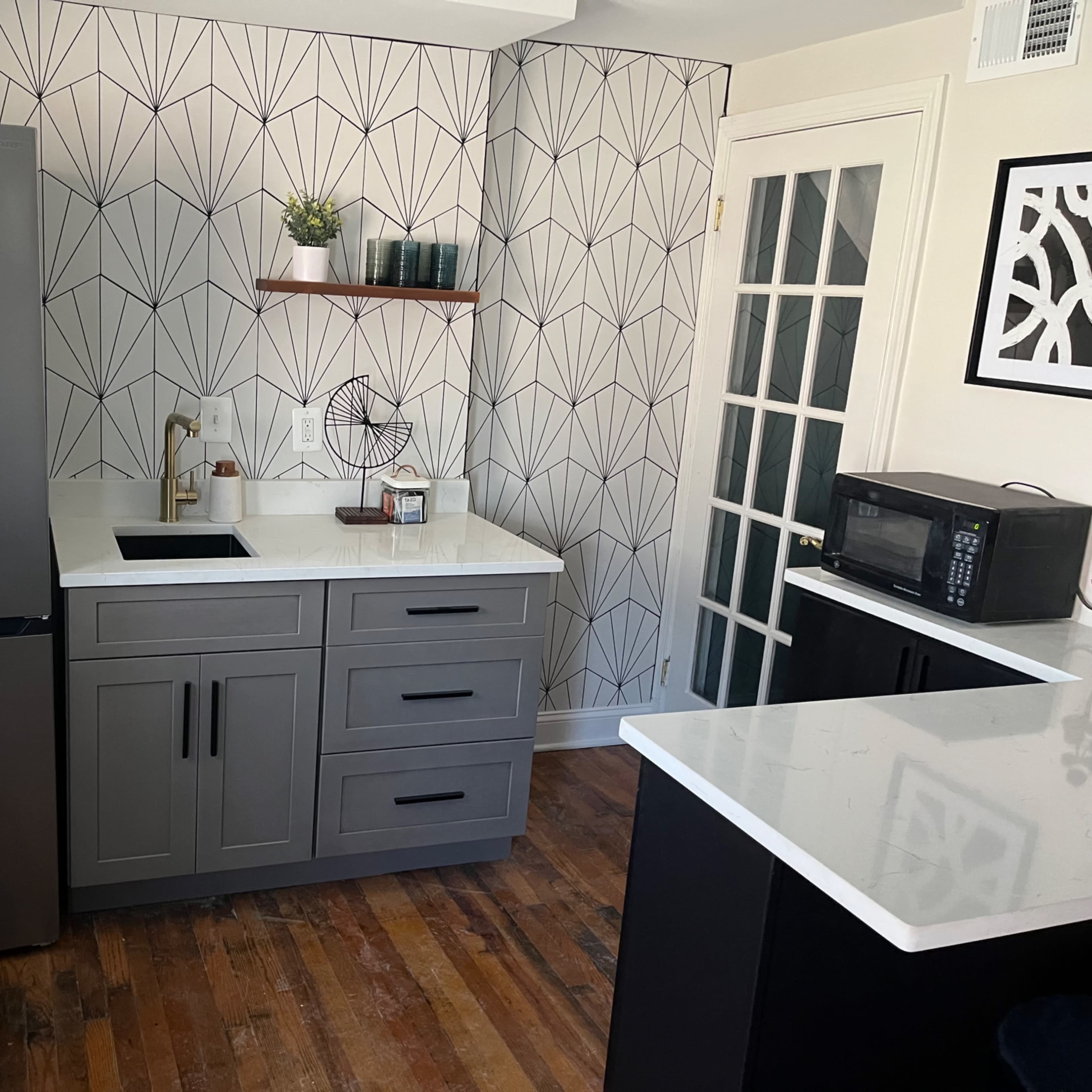 A kitchen features gray cabinetry, a stainless steel refrigerator, a microwave, and a patterned wall design.