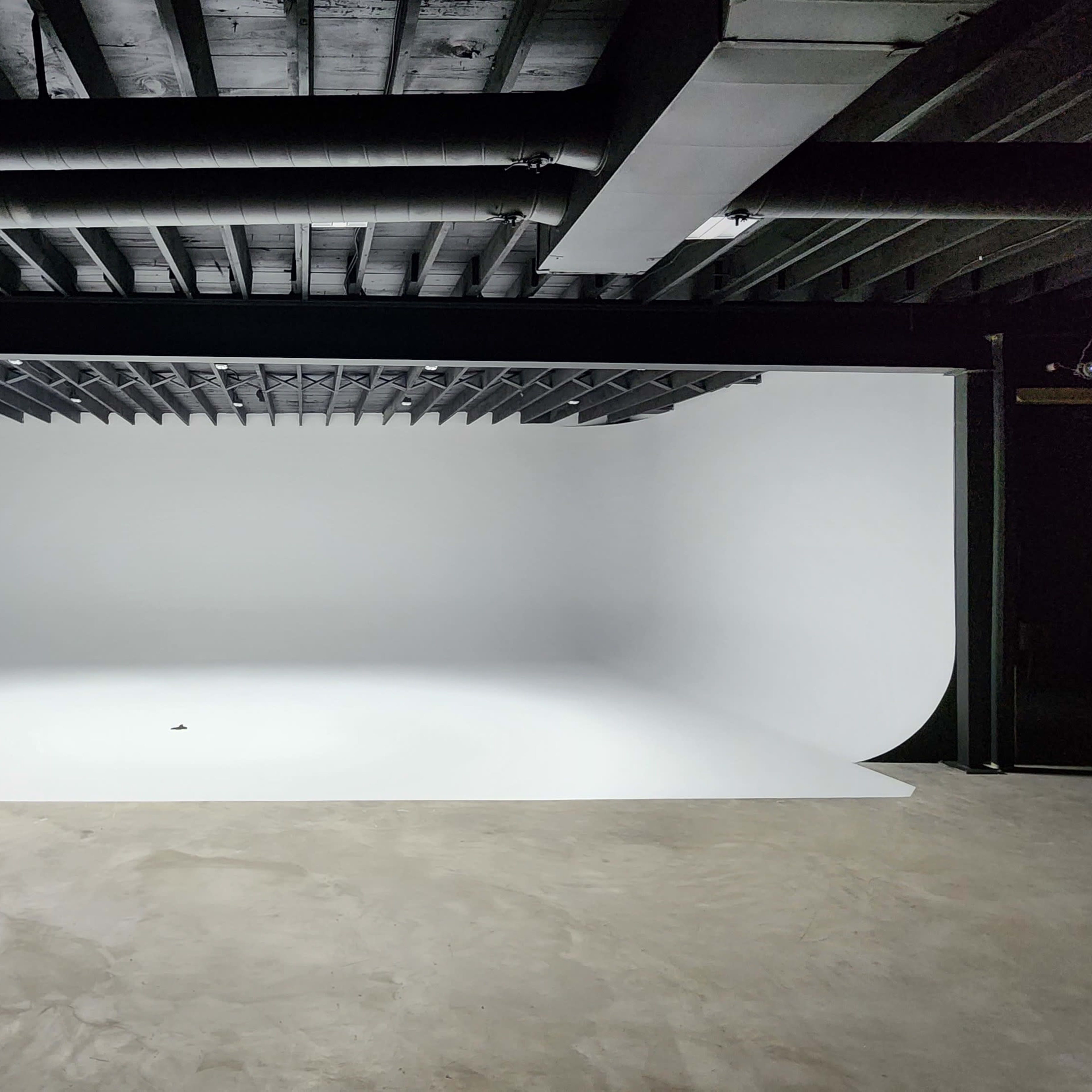 A spacious studio with a seamless white backdrop and concrete flooring.