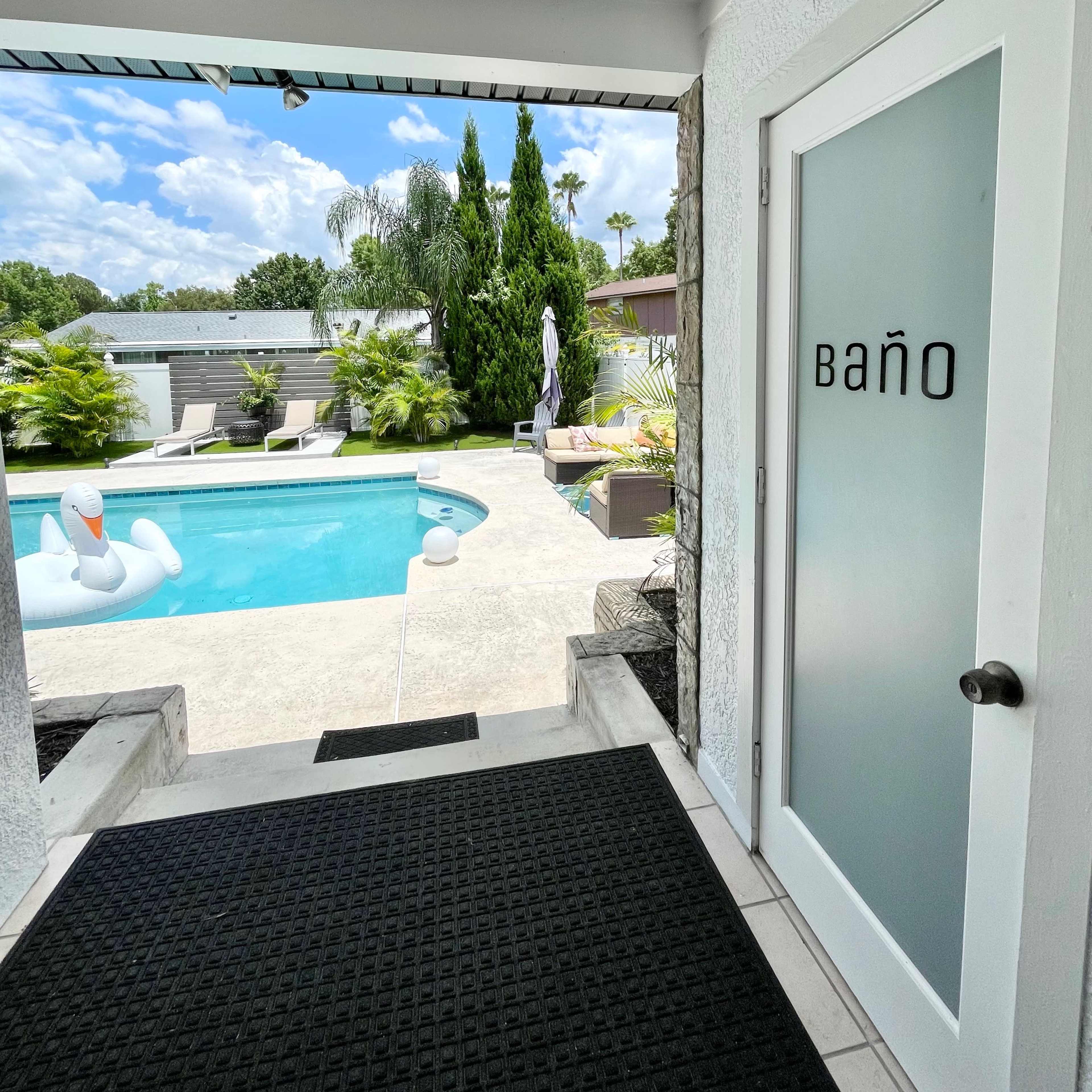 A large inflatable swan floats on a clear blue swimming pool surrounded by palm trees and a modern backyard.