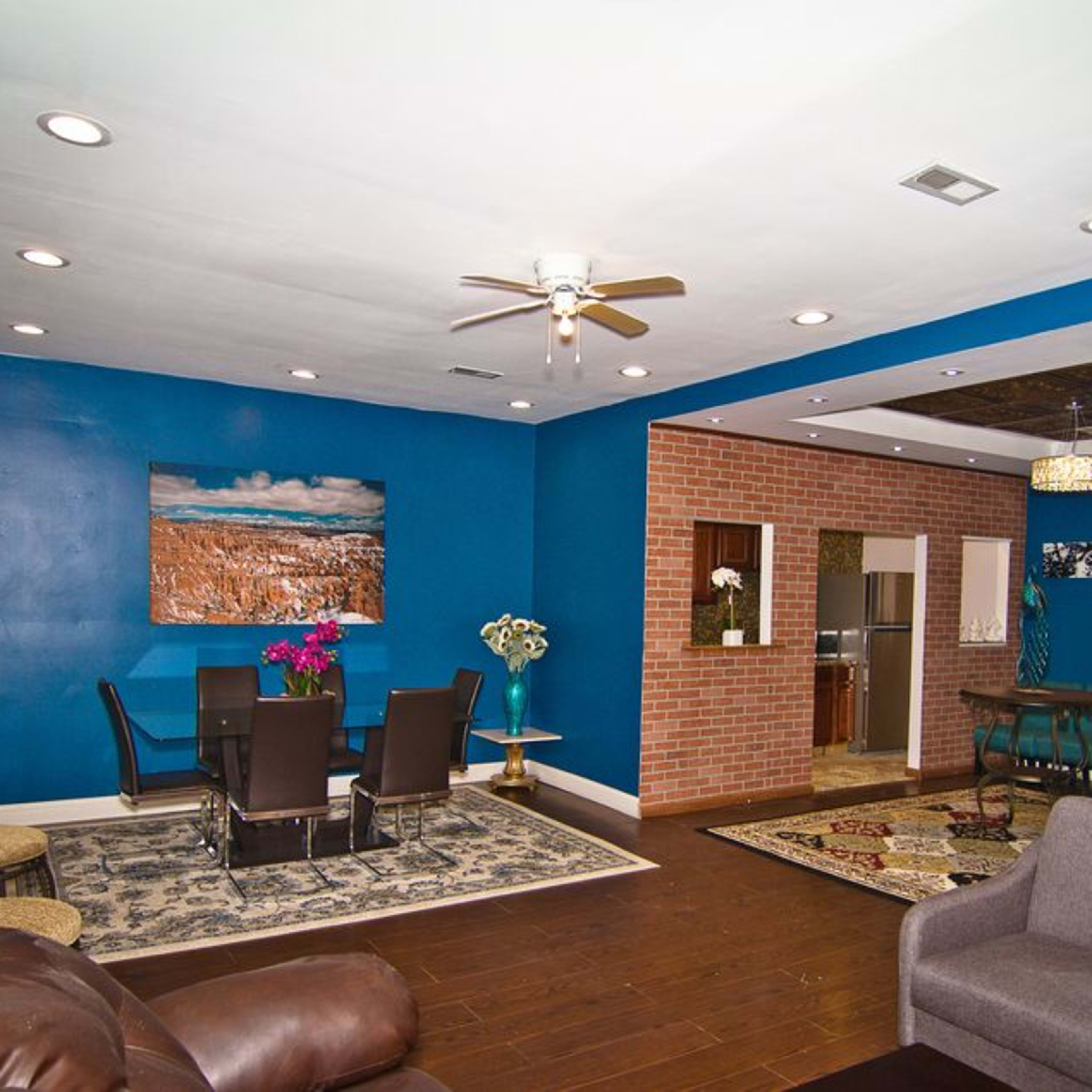 A living space with blue walls, hardwood floors, a dining area with dark chairs and a table, and a kitchen visible in the background.