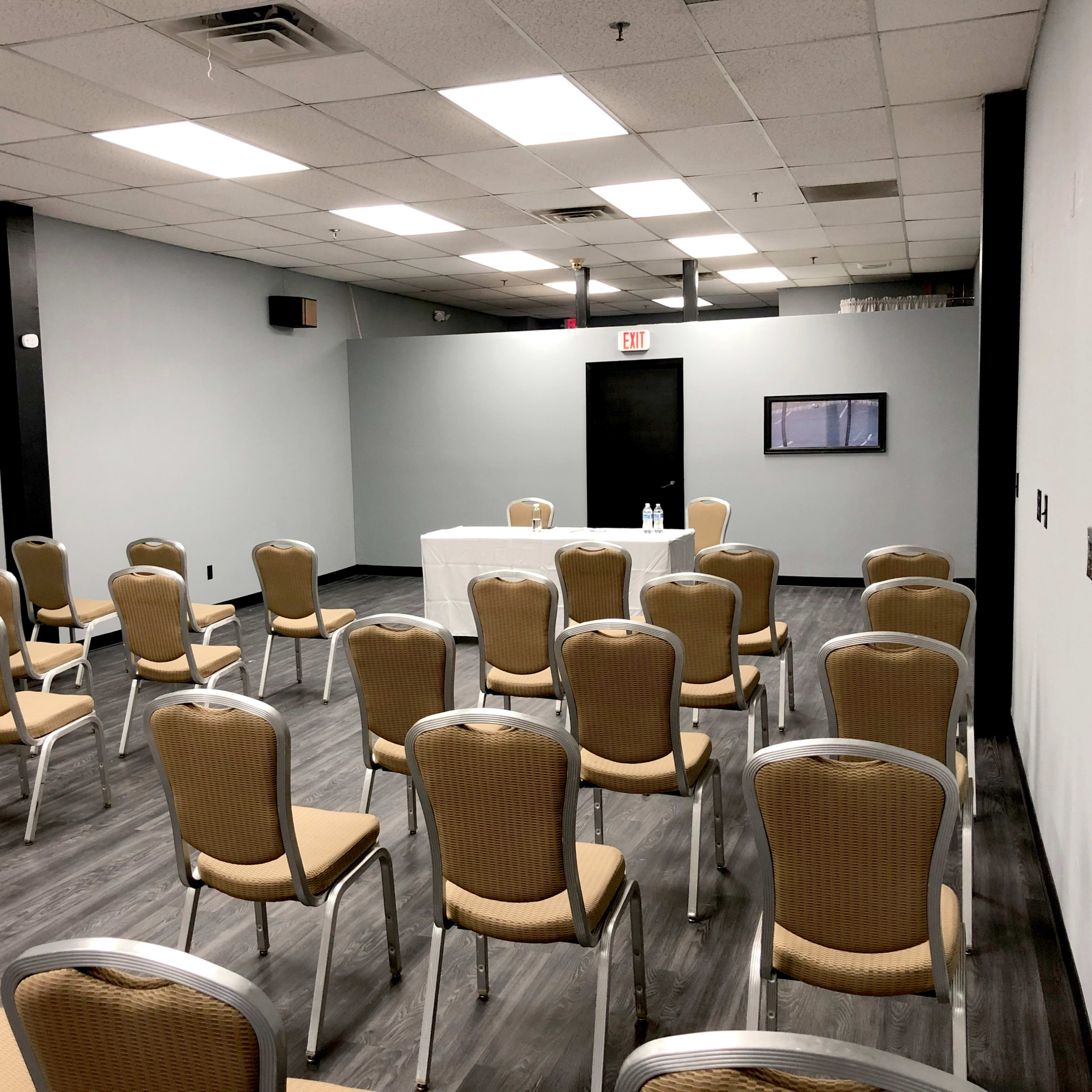 A rectangular room with a table at the front, surrounded by several rows of empty chairs.