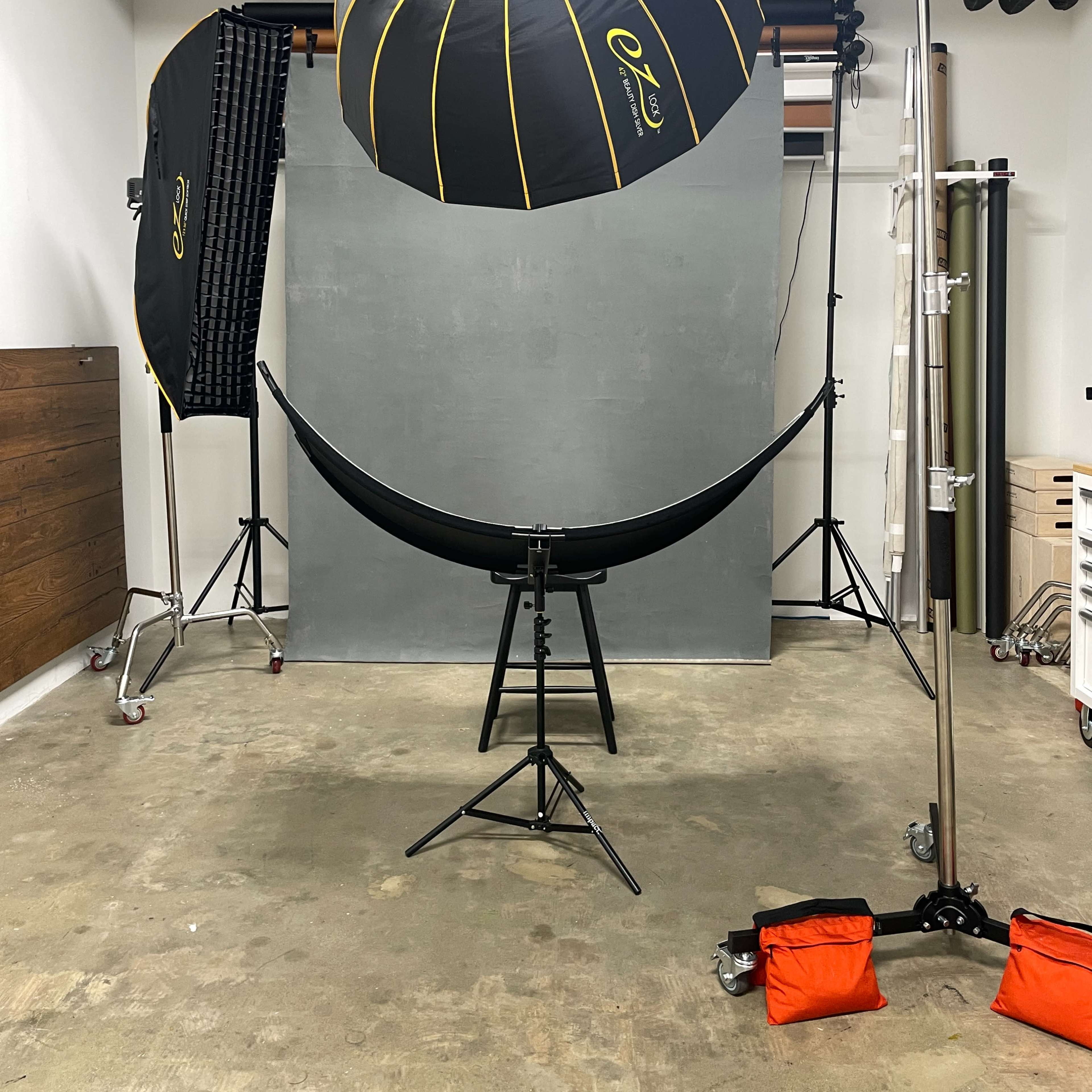 A photography studio setup featuring a gray backdrop, softbox lighting, and a curved black reflector positioned on a stand.