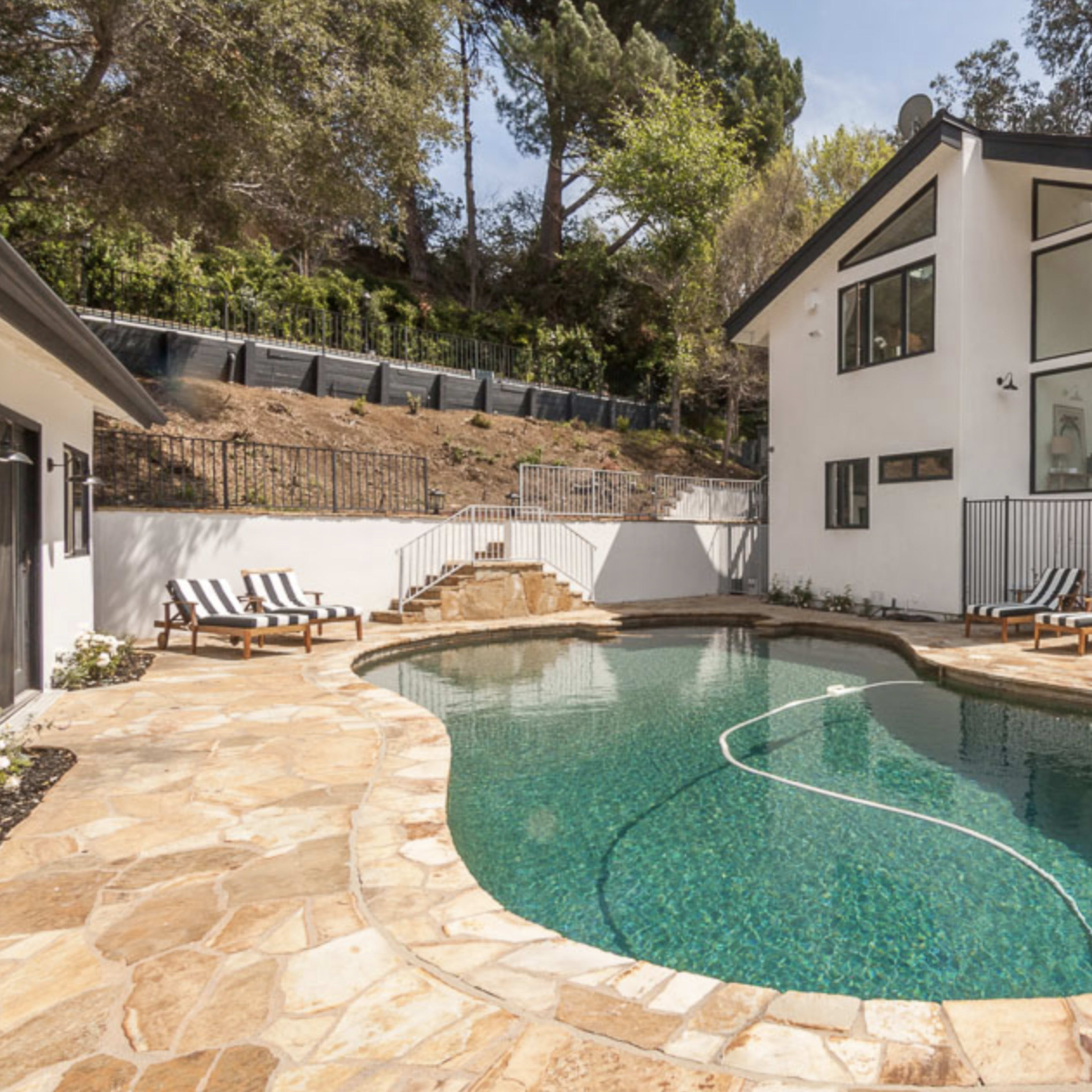 A modern white house beside a curved swimming pool surrounded by stone decking and lounge chairs.