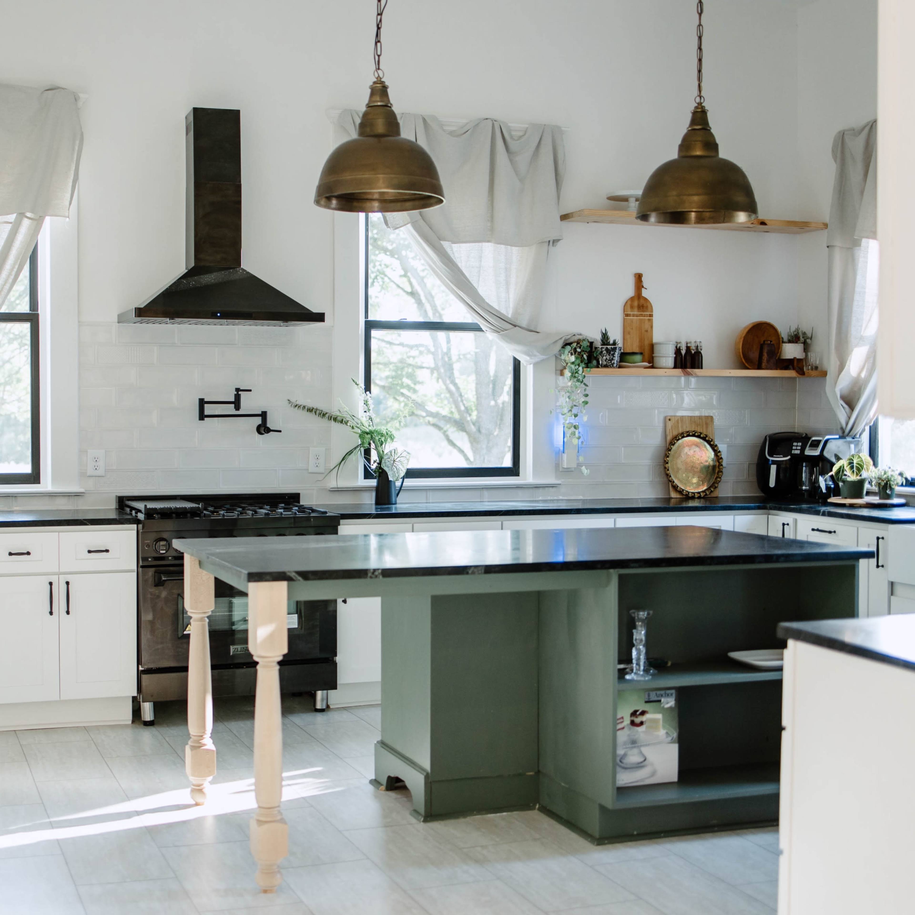 The kitchen features a central island with a dark green base, white cabinetry, and brass pendant lights hanging above.