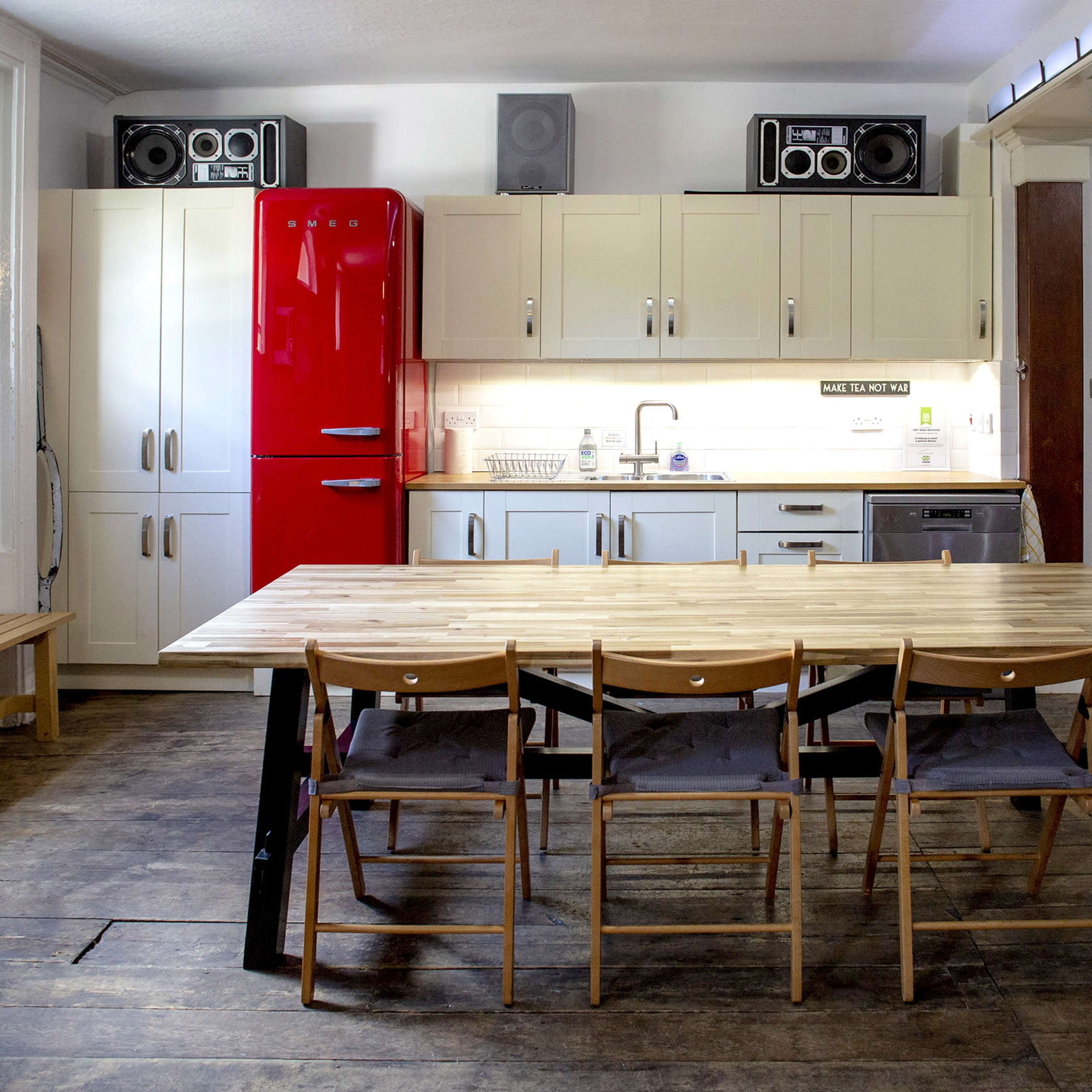 A spacious kitchen features a red refrigerator, a wooden dining table with five chairs, and modern appliances along one wall.
