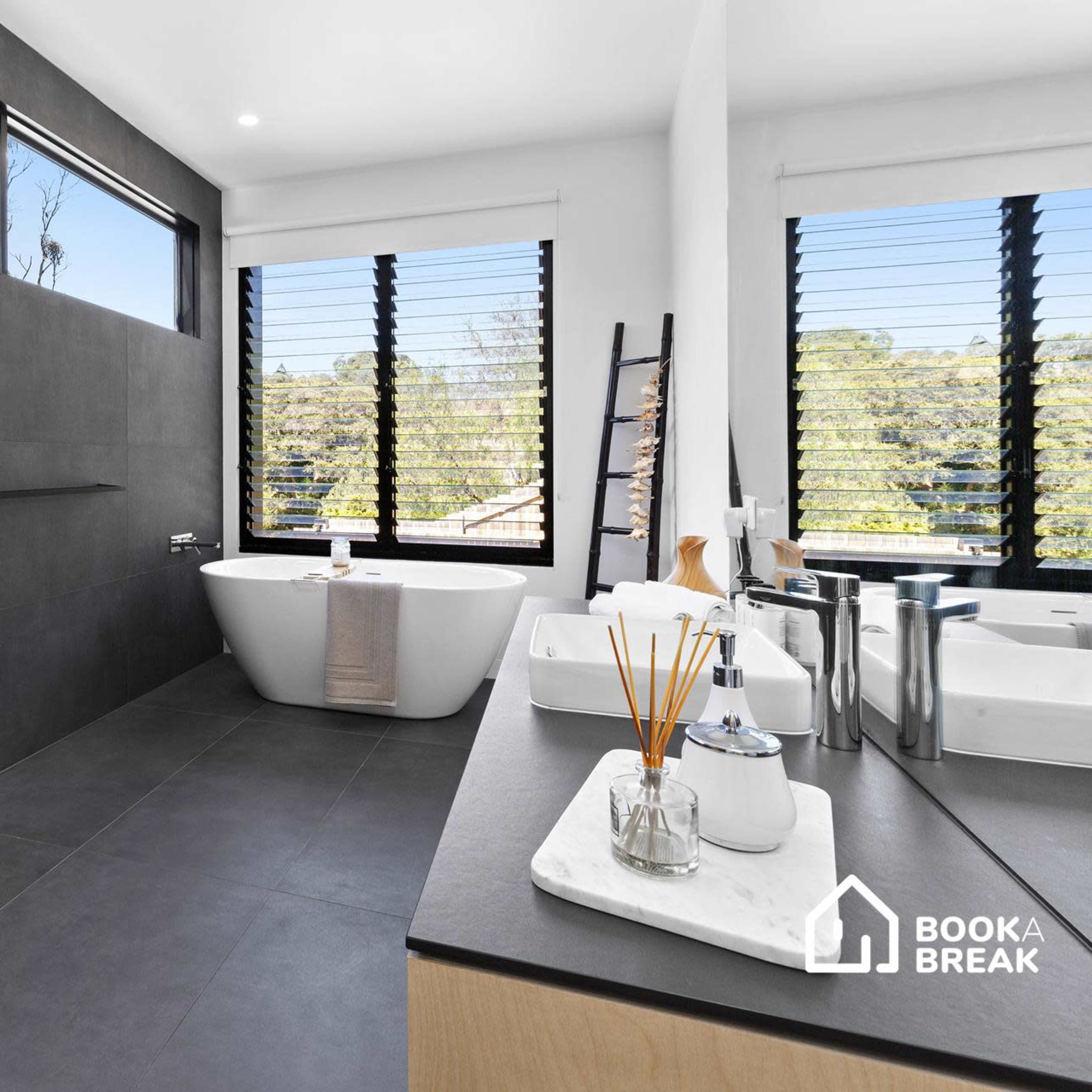 A modern bathroom featuring a freestanding bathtub, a dual sink vanity, and large windows with exterior views.