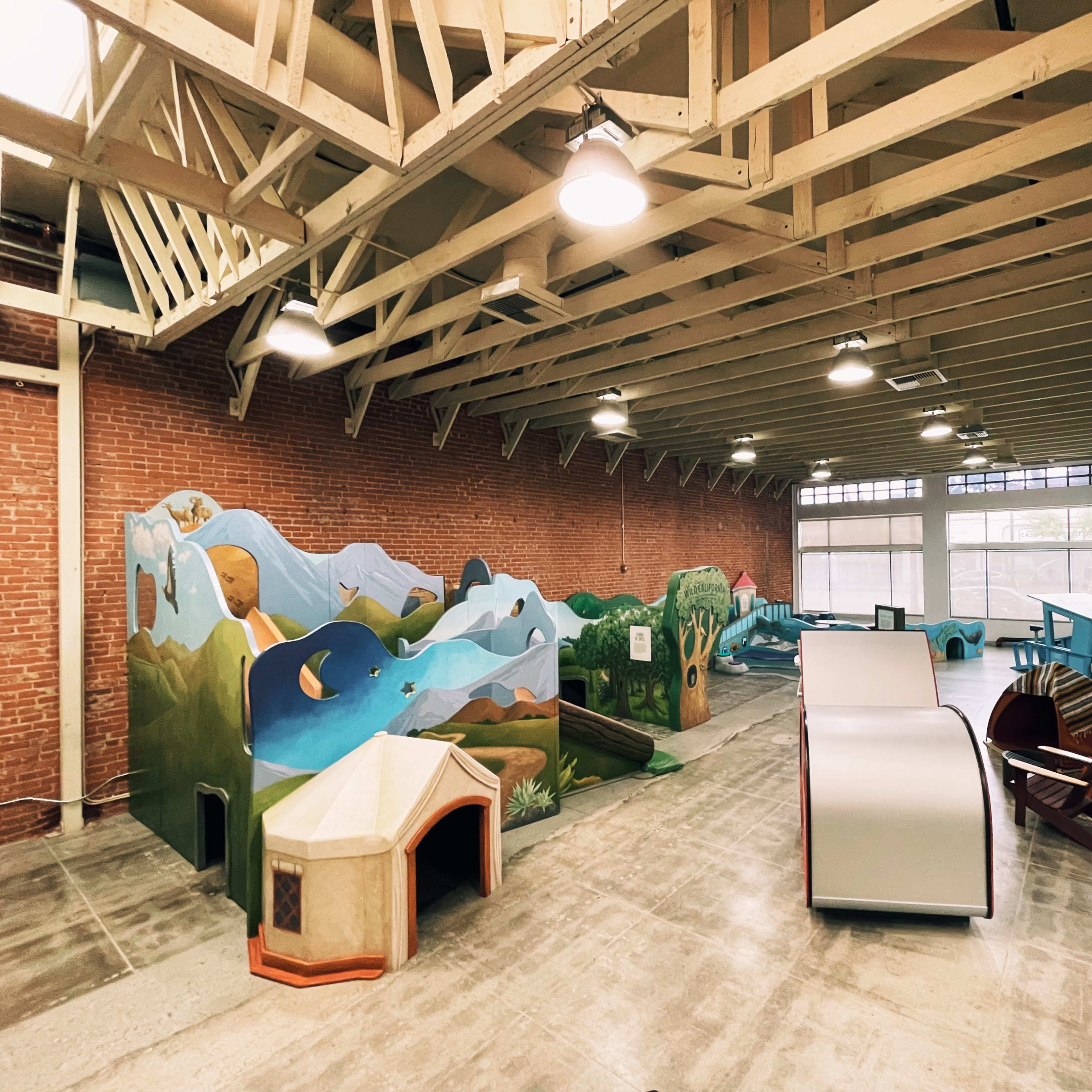 An indoor play area featuring colorful, themed structures and murals, with a spacious layout under a wooden beam ceiling.