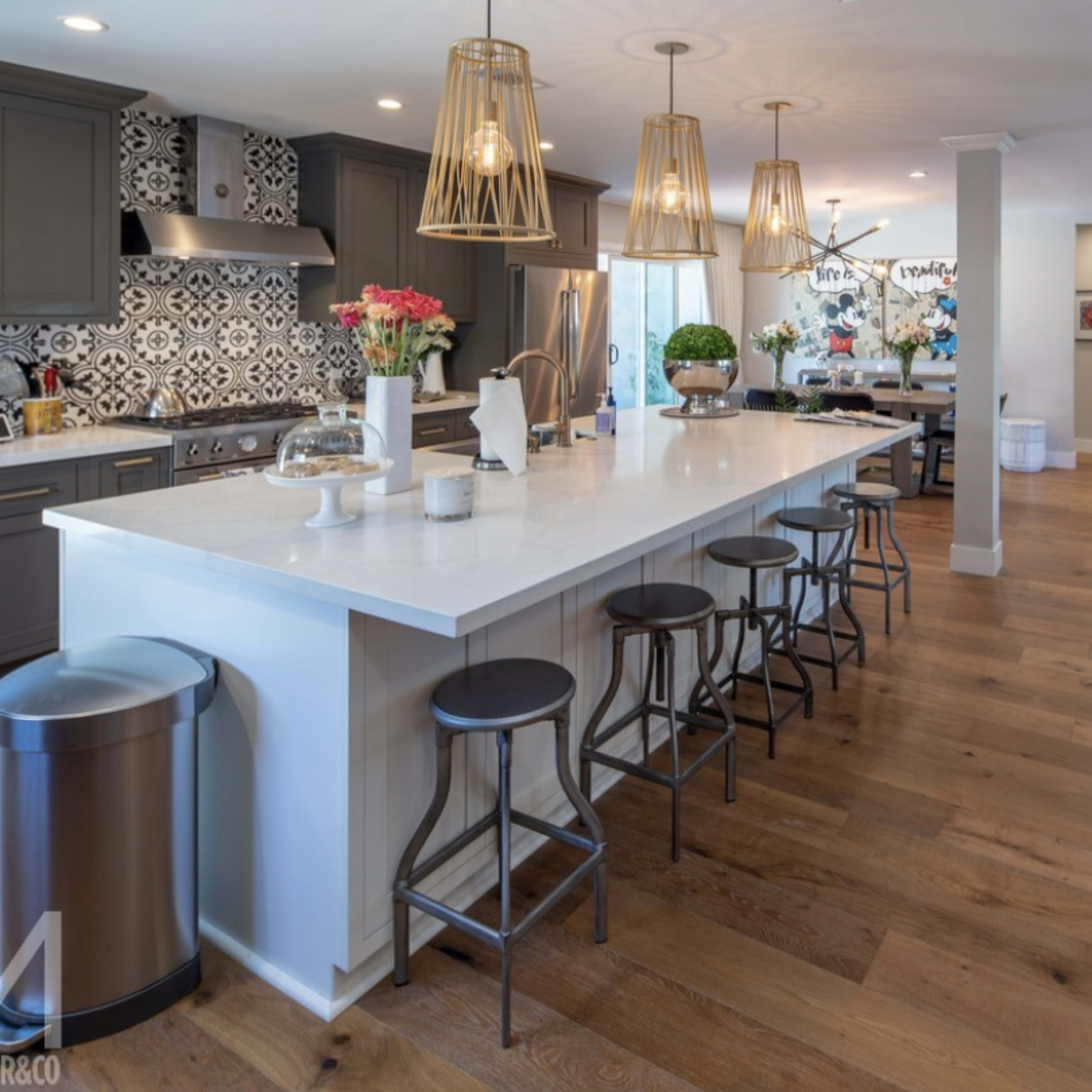 A spacious kitchen features a large island with bar stools, modern cabinetry, and decorative tile backsplash.