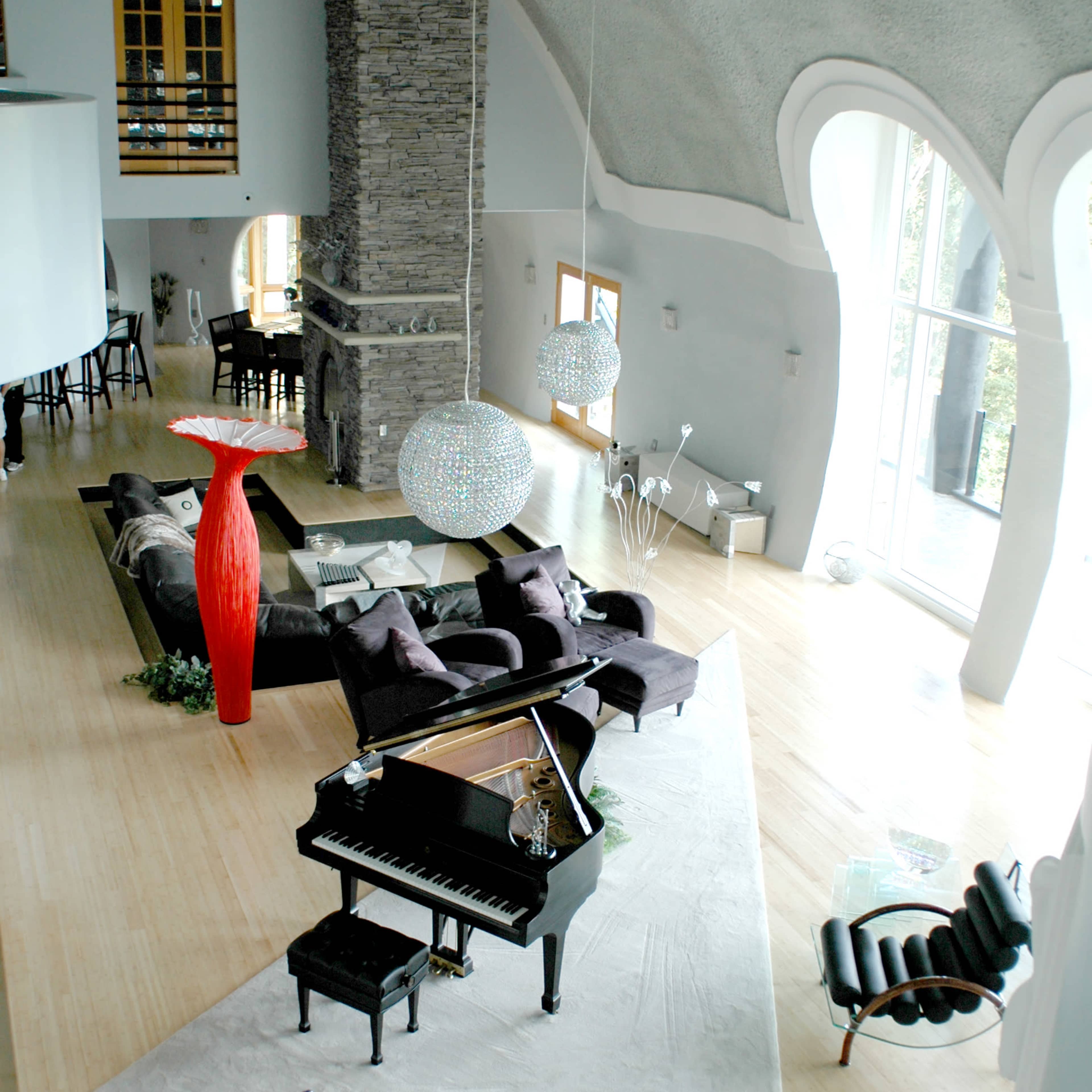 A spacious, modern living room featuring a grand piano, elegant furniture, and large windows with natural light.