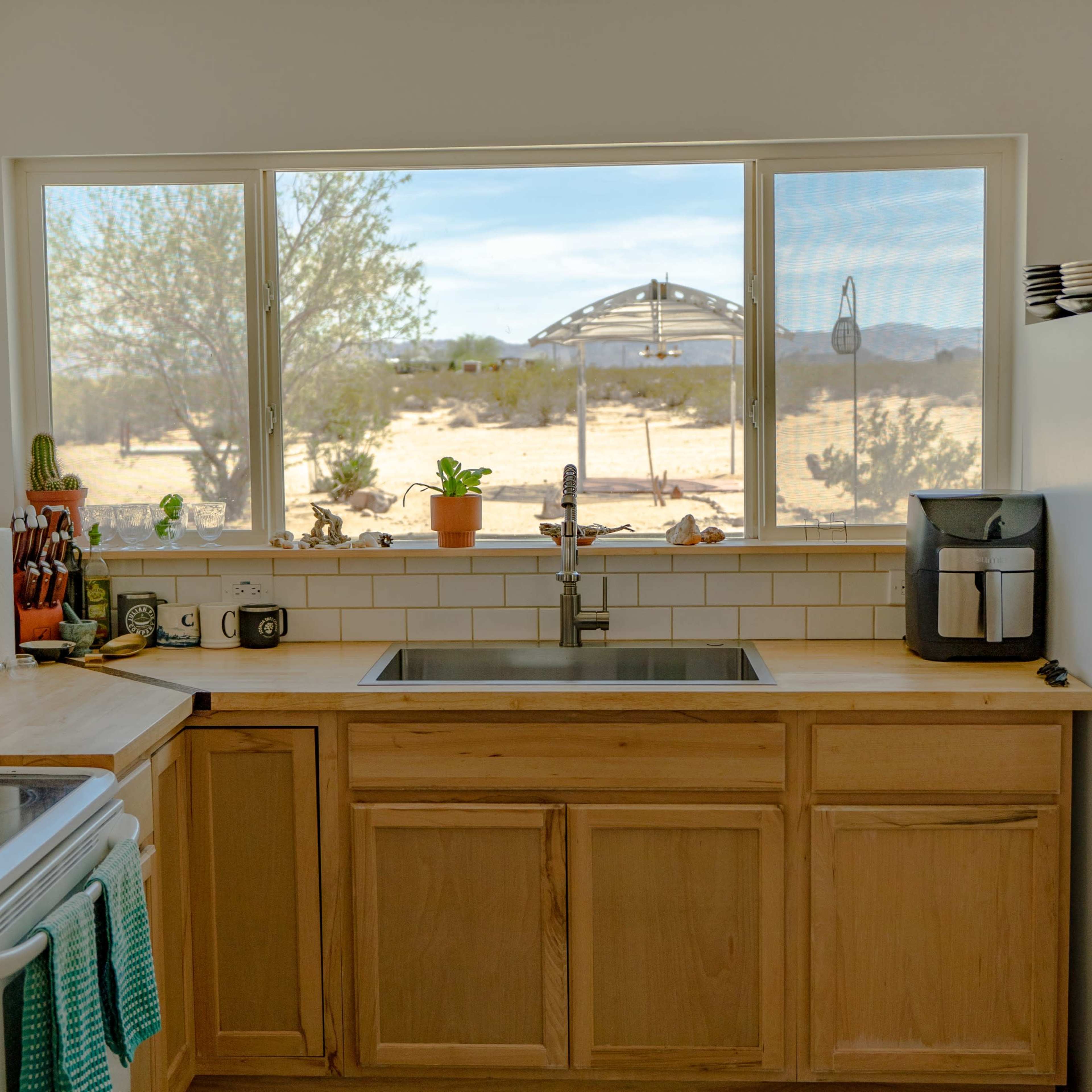 A clean kitchen with wooden cabinets and a window overlooking a desert landscape.