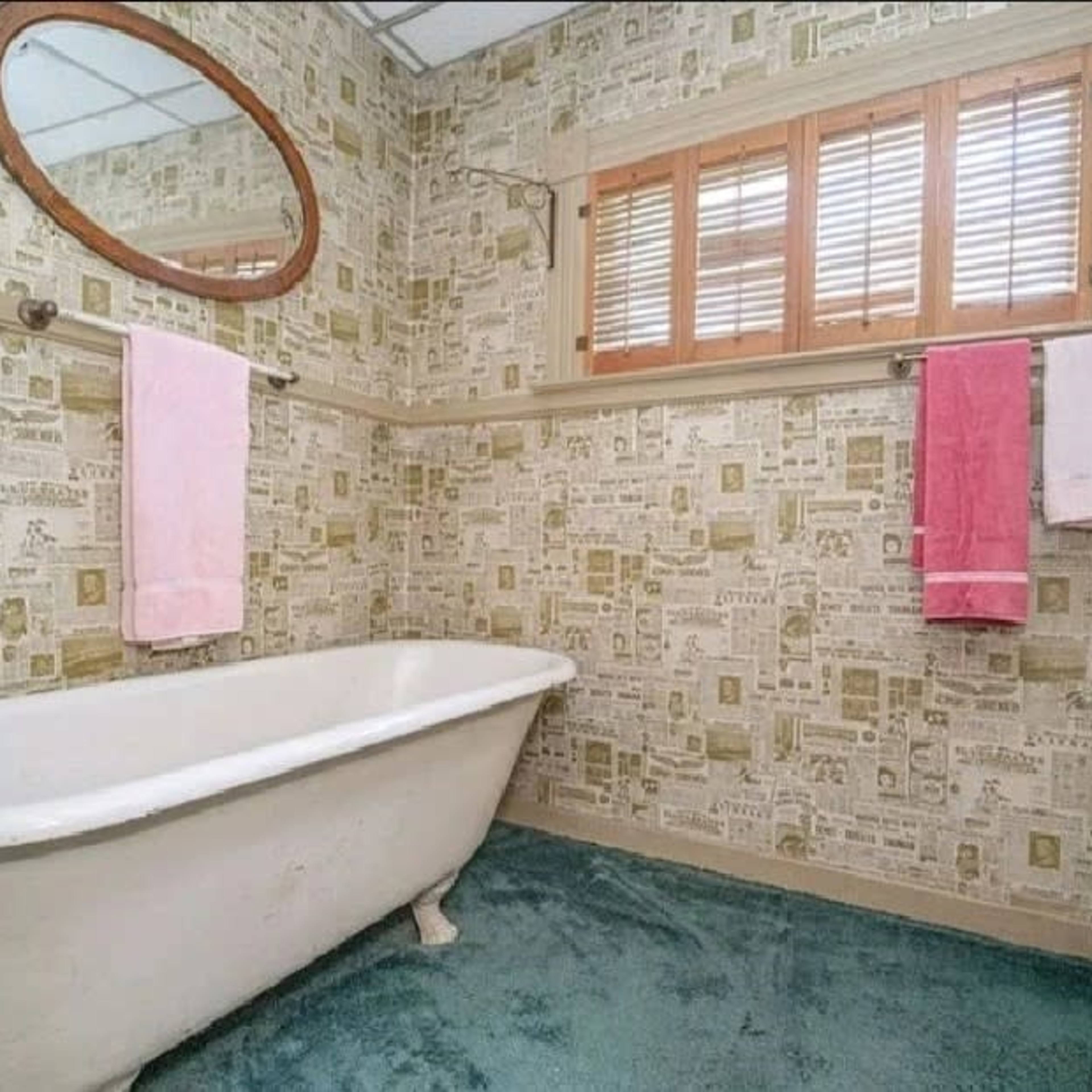 The bathroom features a clawfoot tub, patterned wallpaper, and two pink towels hanging on a towel rack.