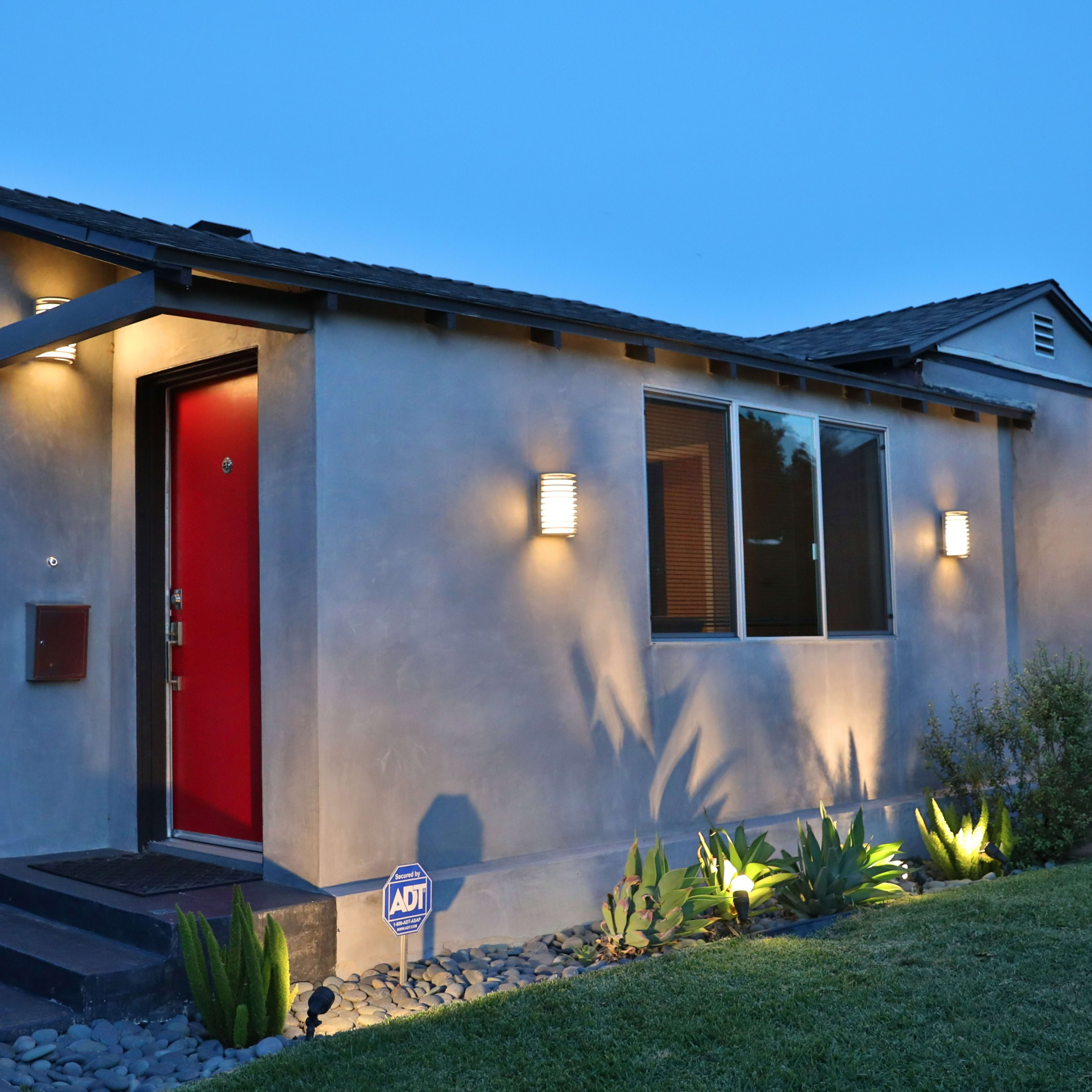 A modern house with a red front door, illuminated by exterior lights, and surrounded by a landscaped yard.
