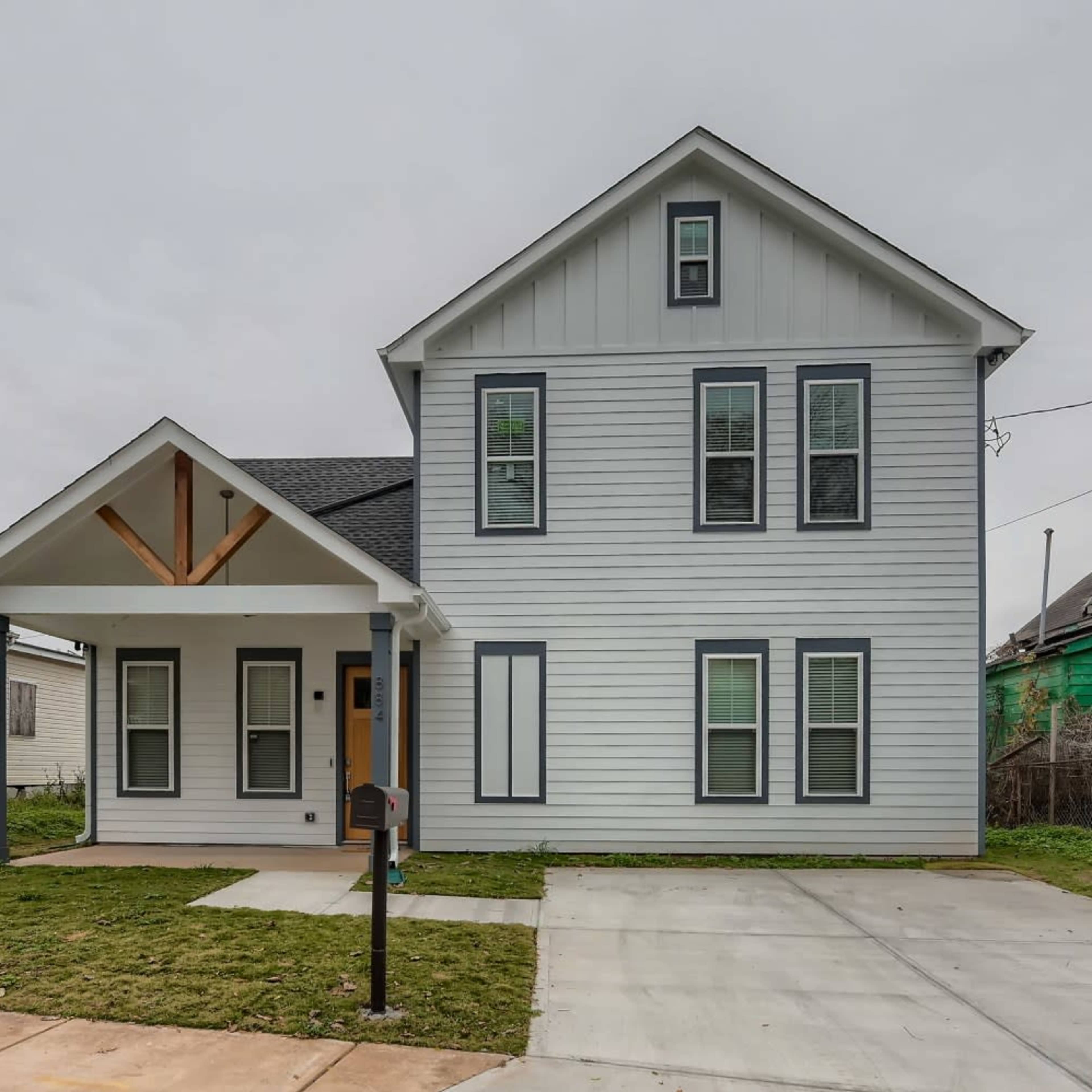 A two-story house with a gray exterior, a front porch supported by two columns, and a concrete driveway.