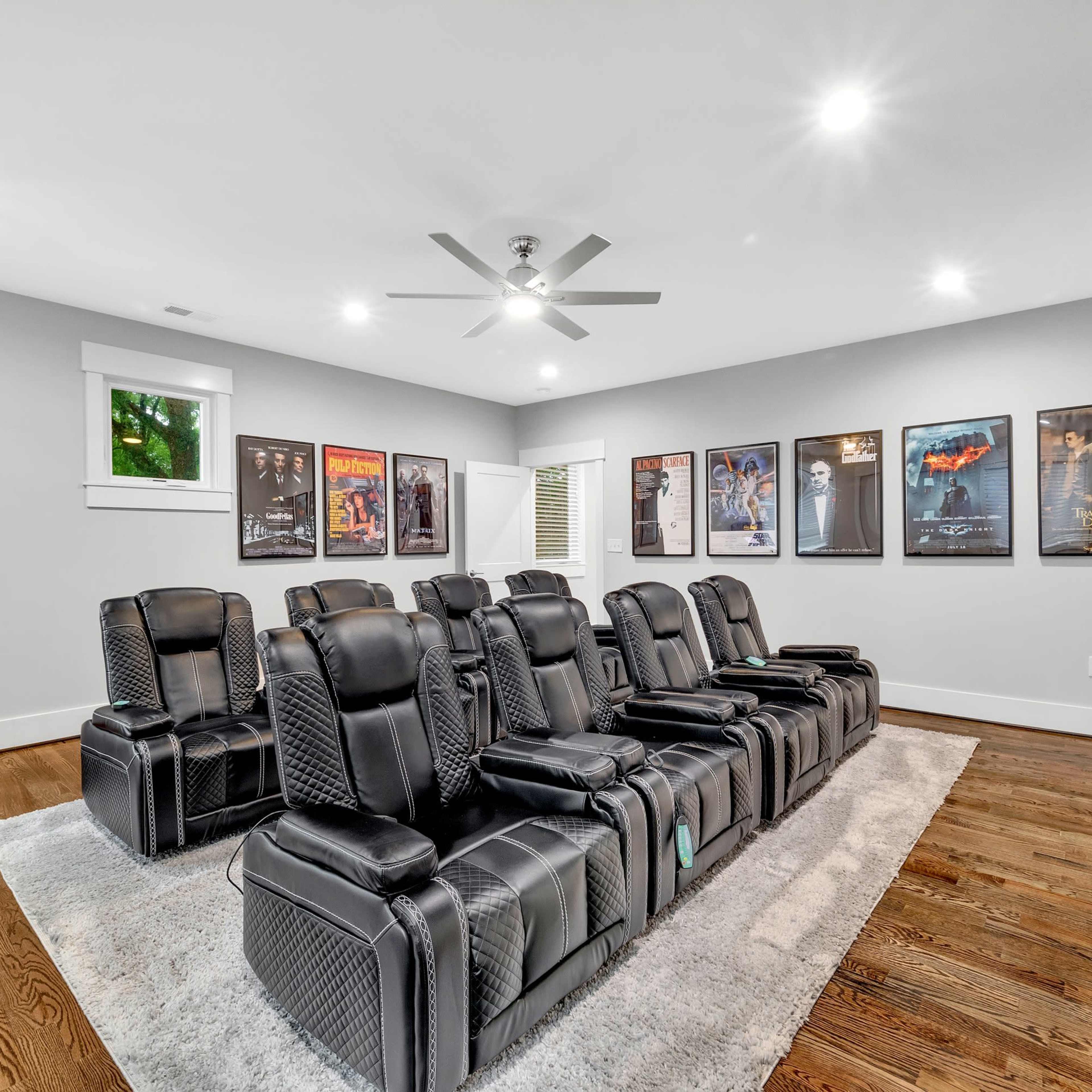 A home theater room with black reclining chairs, a gaming arcade machine, and framed movie posters on the walls.