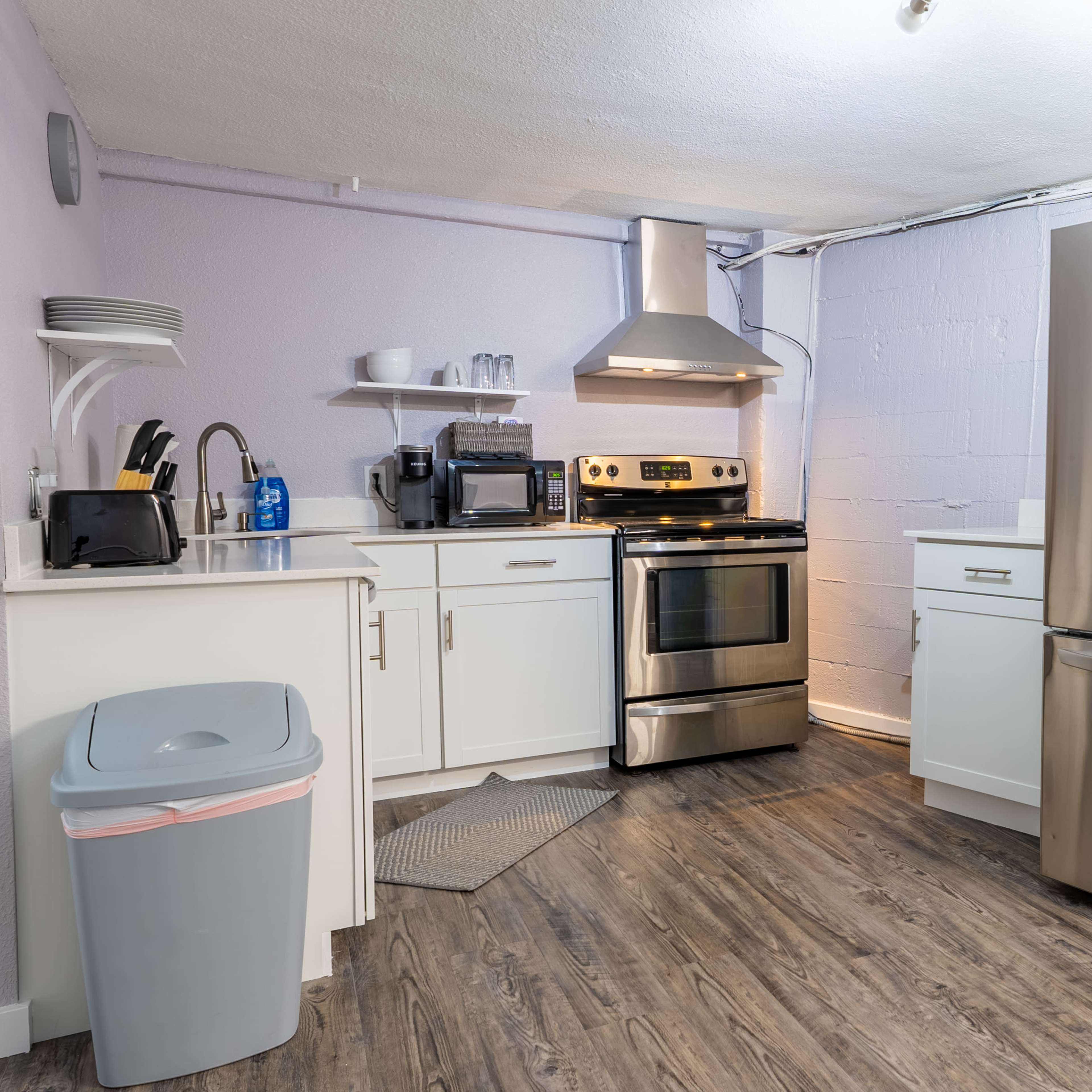 A modern kitchen with stainless steel appliances, including a refrigerator and oven, set against light purple walls and wood-like flooring.