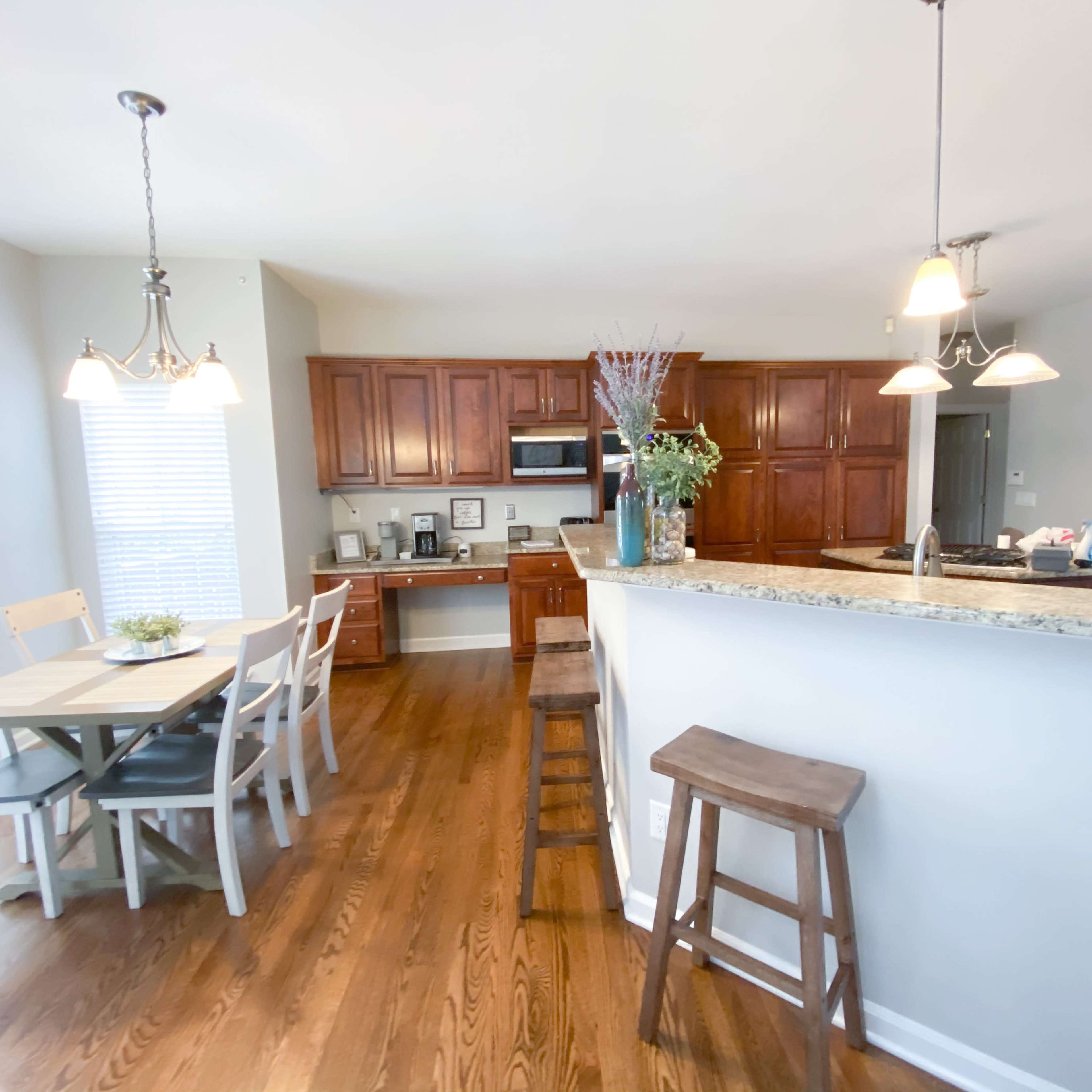 A kitchen and dining area with wooden cabinets, a granite countertop, a table and chairs, and bar stools.