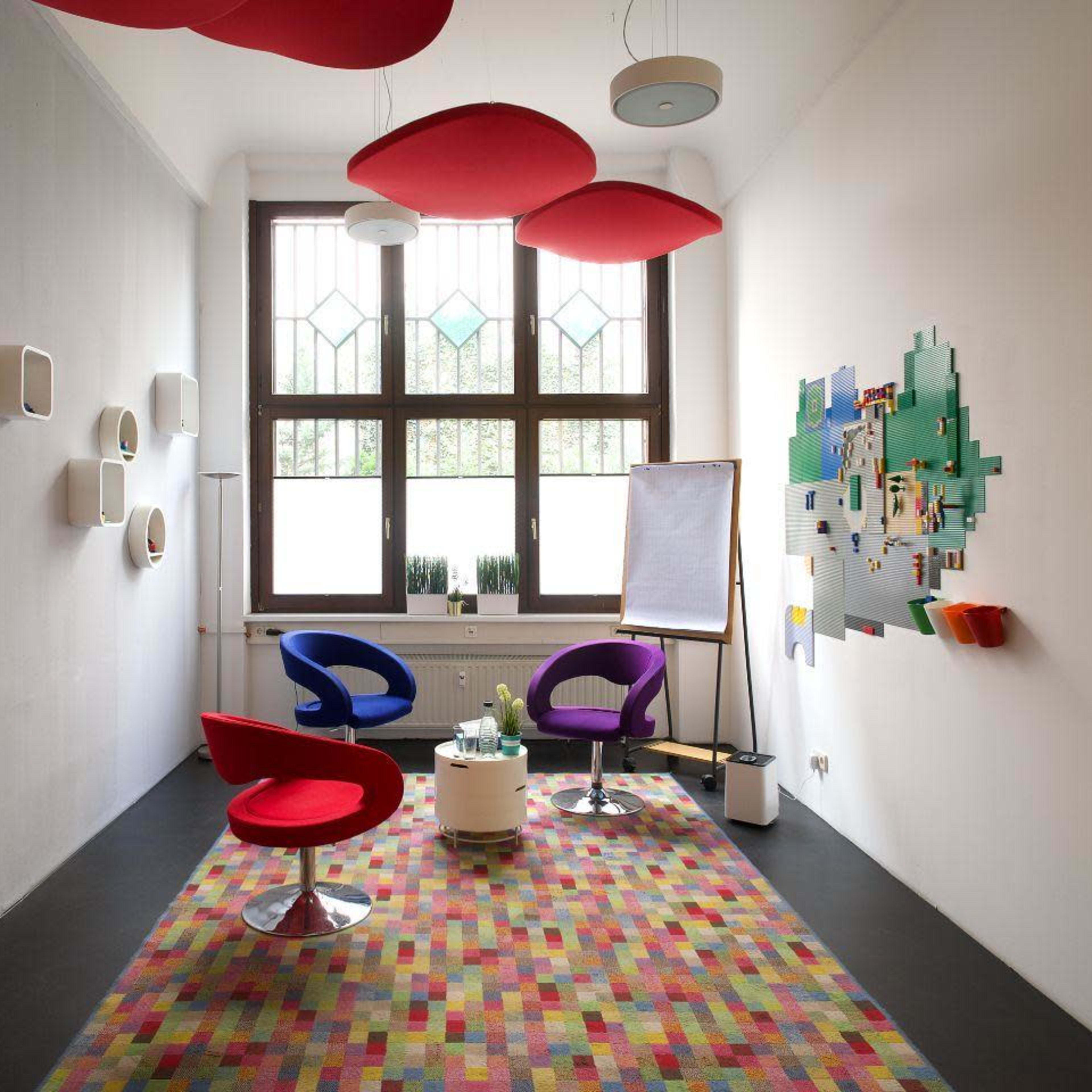 A modern meeting room features colorful furniture, a patterned rug, and large windows providing natural light.
