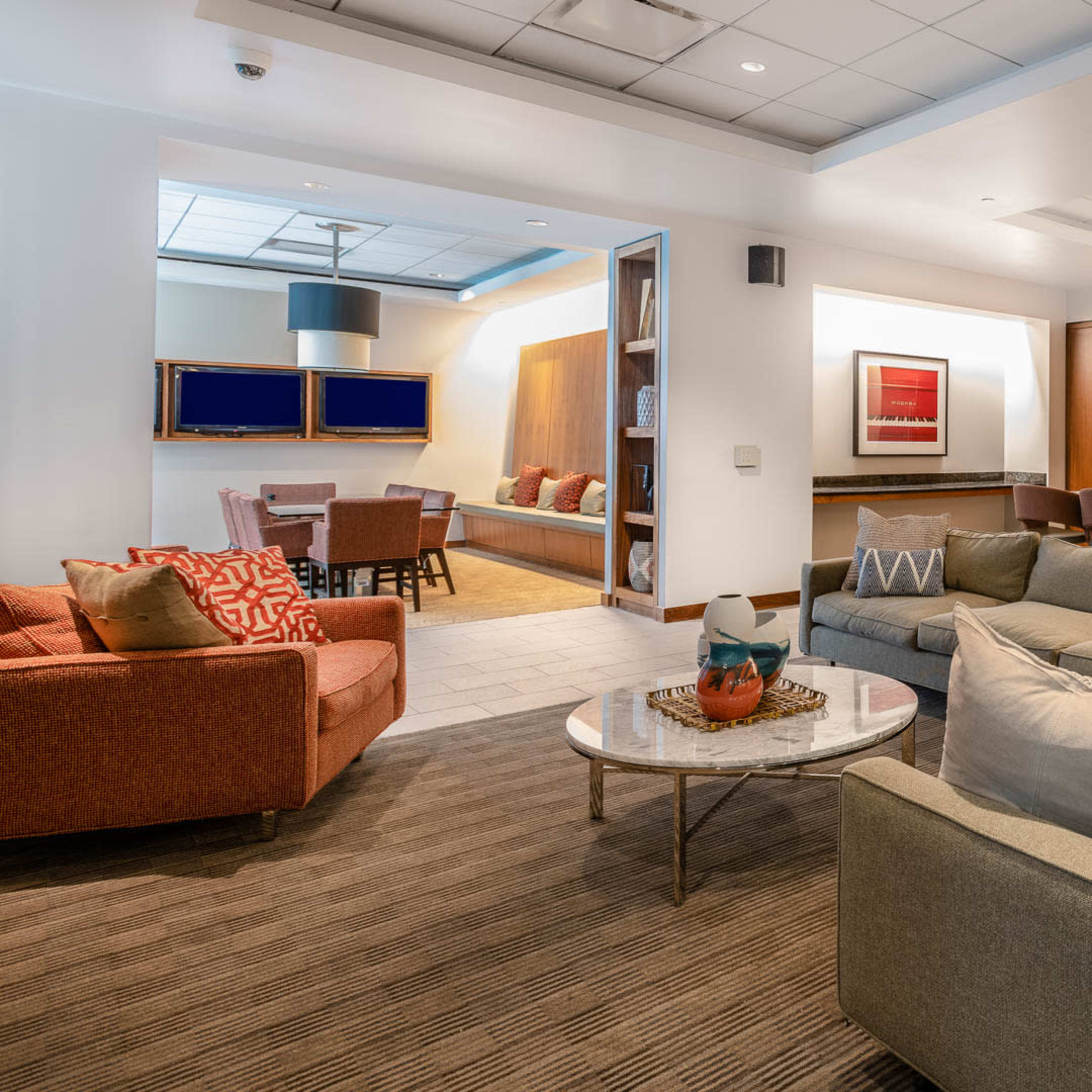 A modern lounge area featuring two sofas, a coffee table, and a kitchen with bar seating and appliances.