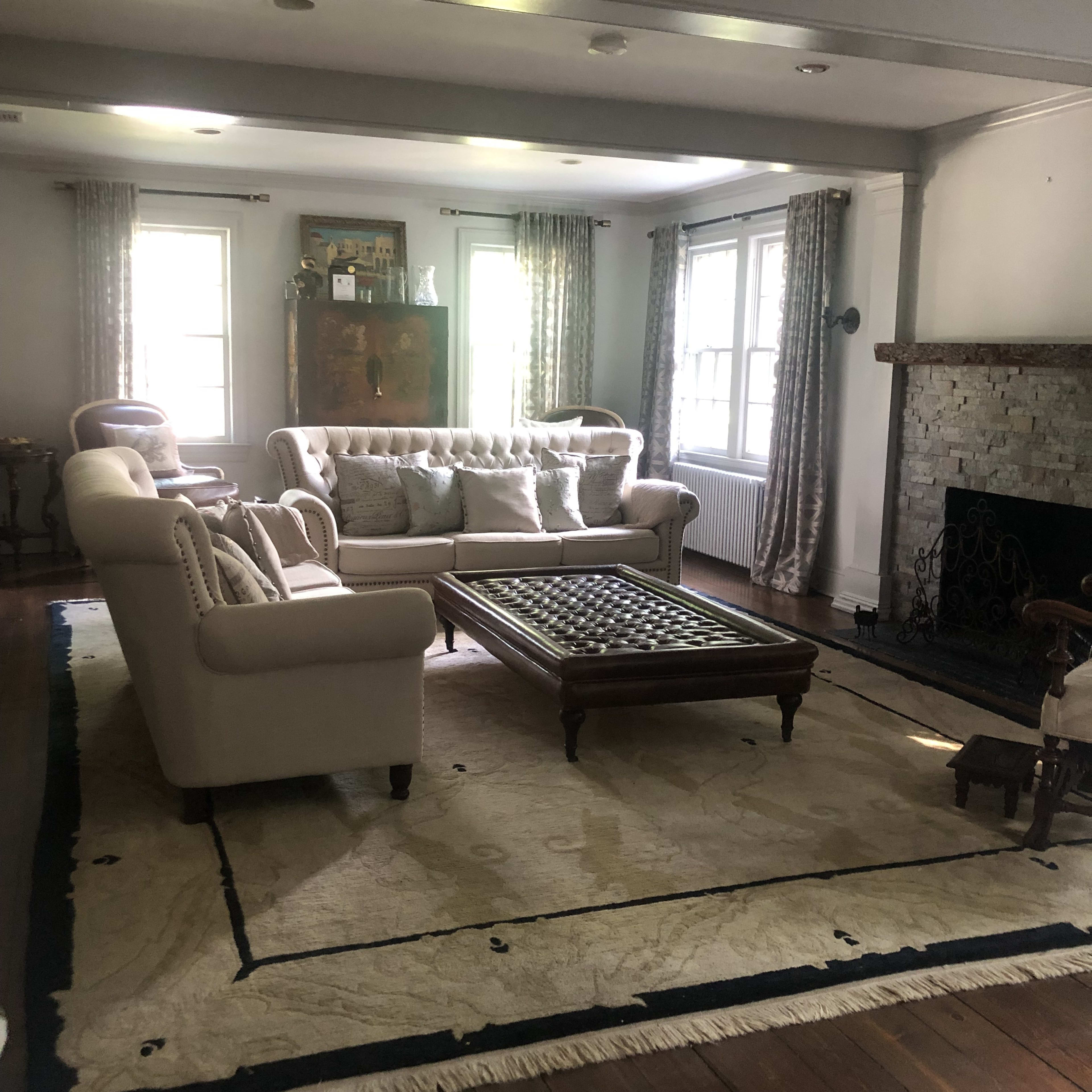 A living room with a light-colored sofa, a wooden coffee table, and a stone fireplace, all arranged on a large area rug.