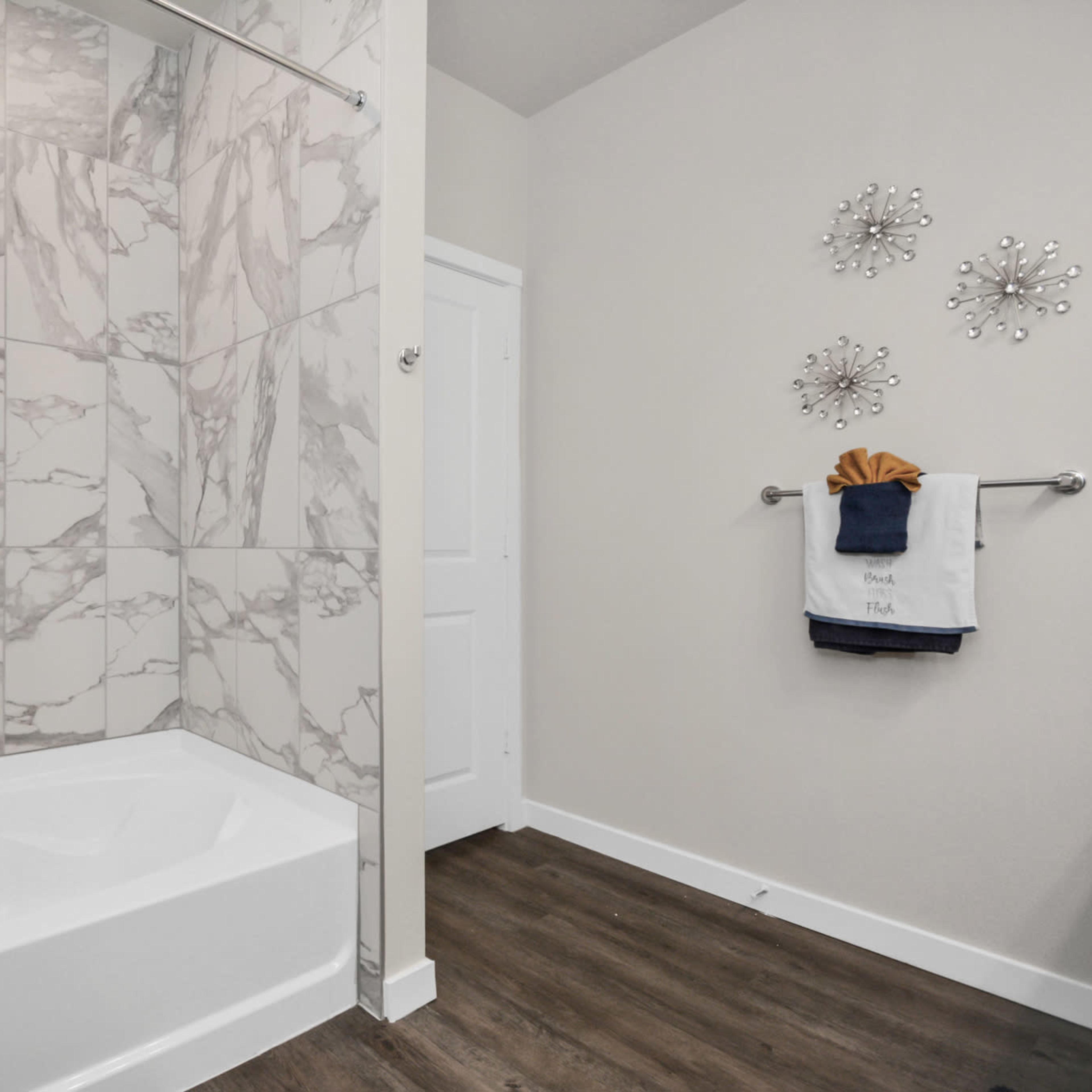 A modern bathroom featuring a white bathtub, marble-patterned wall tiles, and a towel rack with neatly hung towels.
