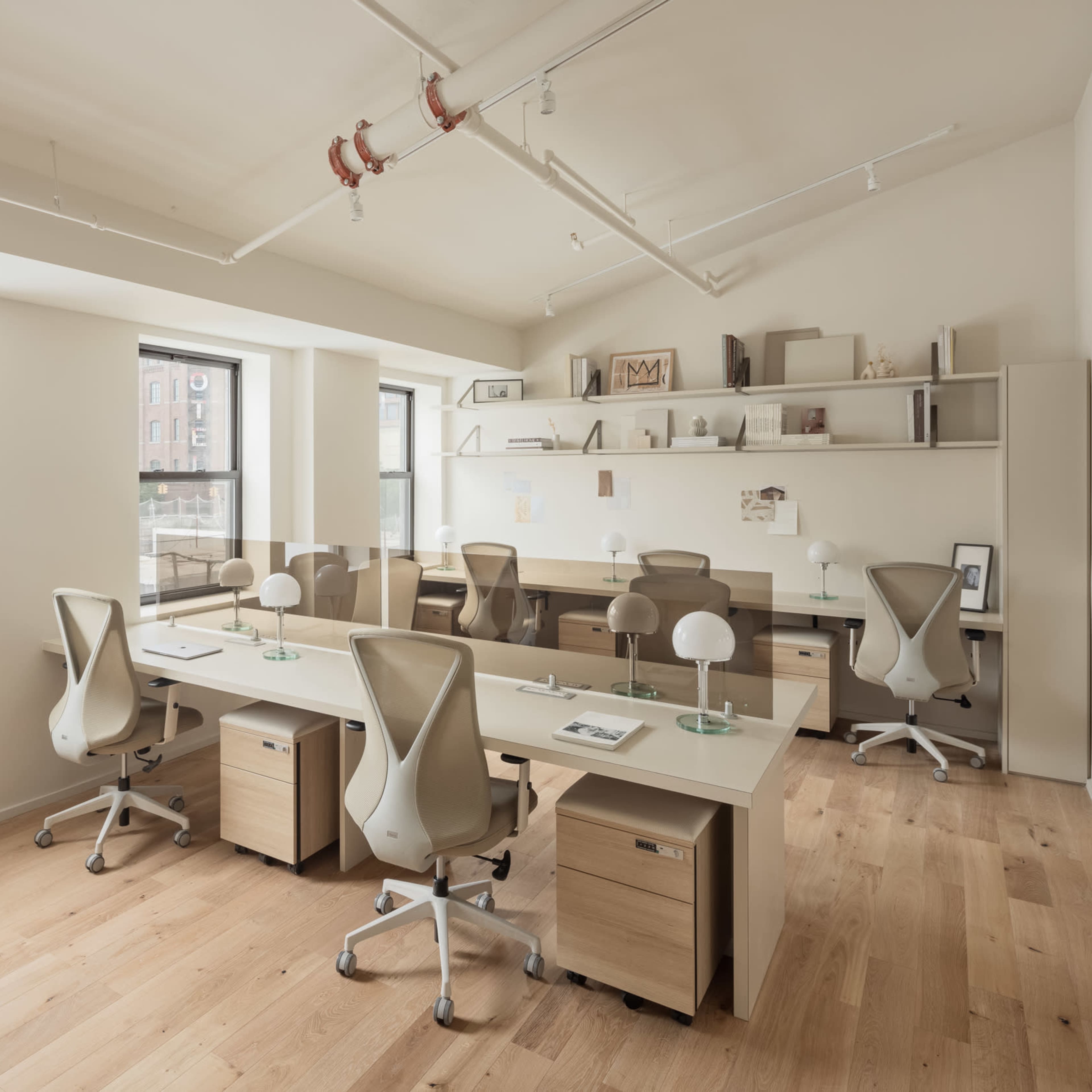 A modern office space with several workstations, large windows, and wooden flooring.