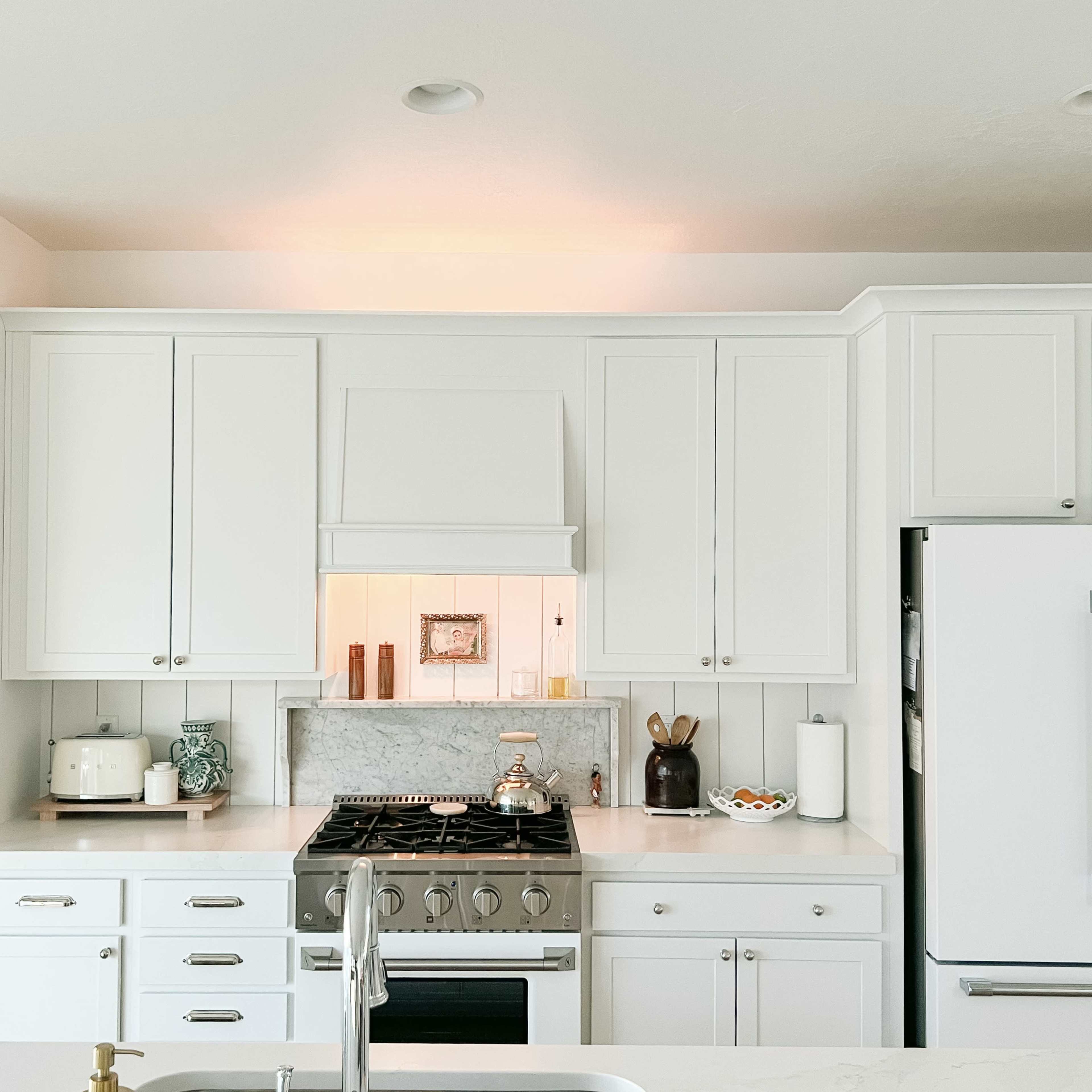 A modern kitchen with white cabinetry, a stainless steel gas stove, and a large refrigerator against a light-colored backsplash.