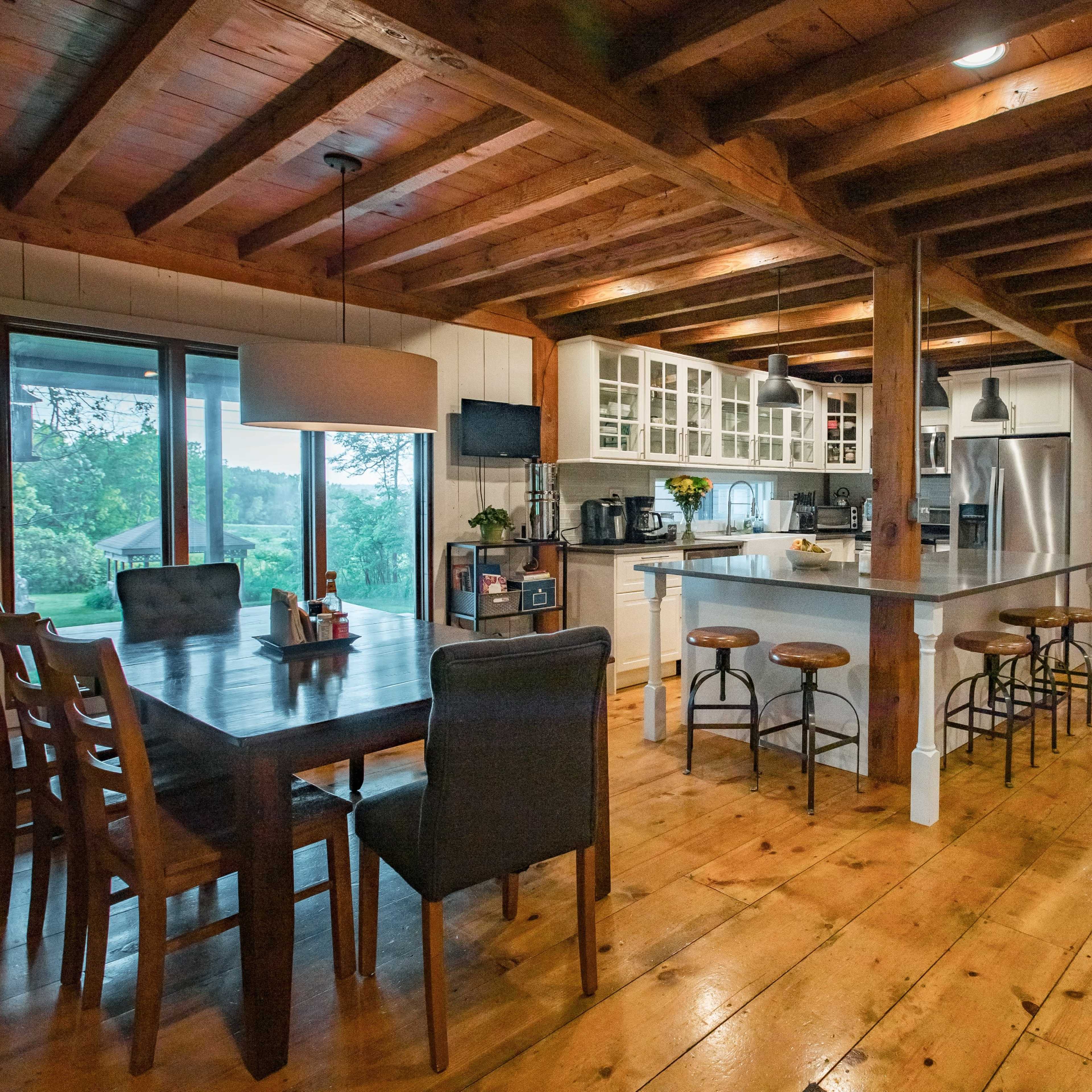 A spacious kitchen and dining area with wooden beams, a large table, and a modern kitchen equipped with stainless steel appliances.