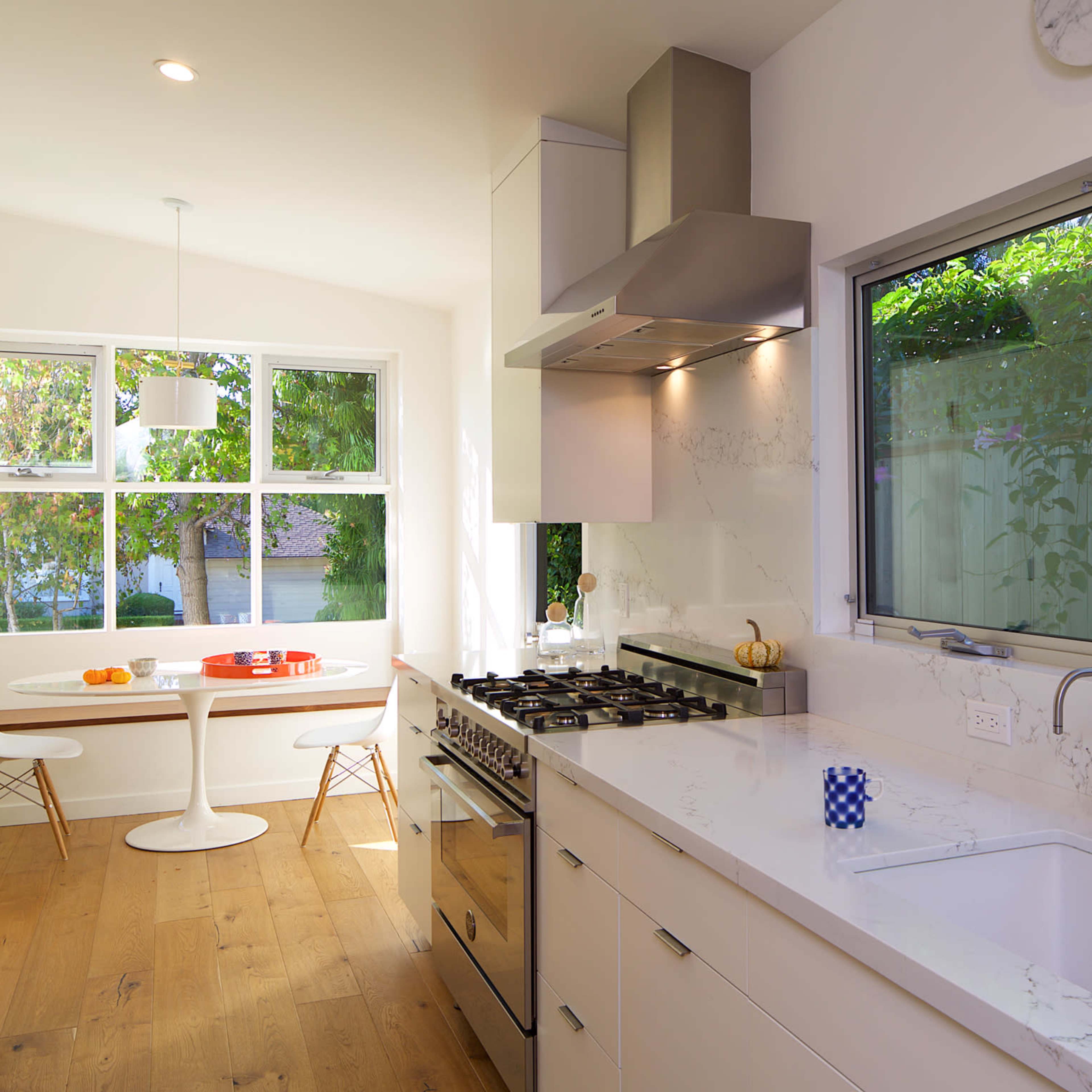 A modern kitchen with a gas stove, white cabinetry, and a dining area featuring a round table and chairs near large windows.