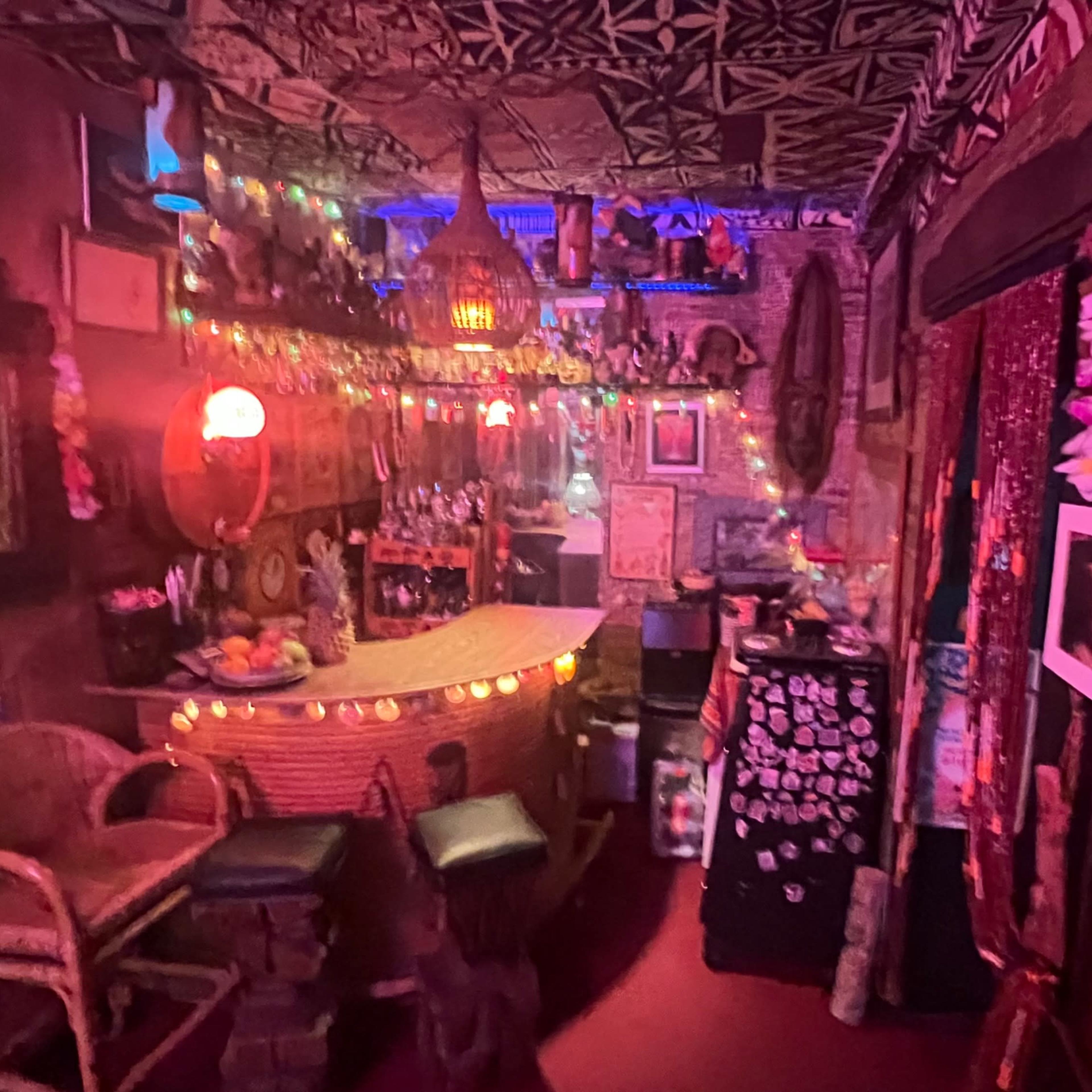 A dimly lit bar area decorated with colorful string lights, tropical decor, and various artworks lining the walls.